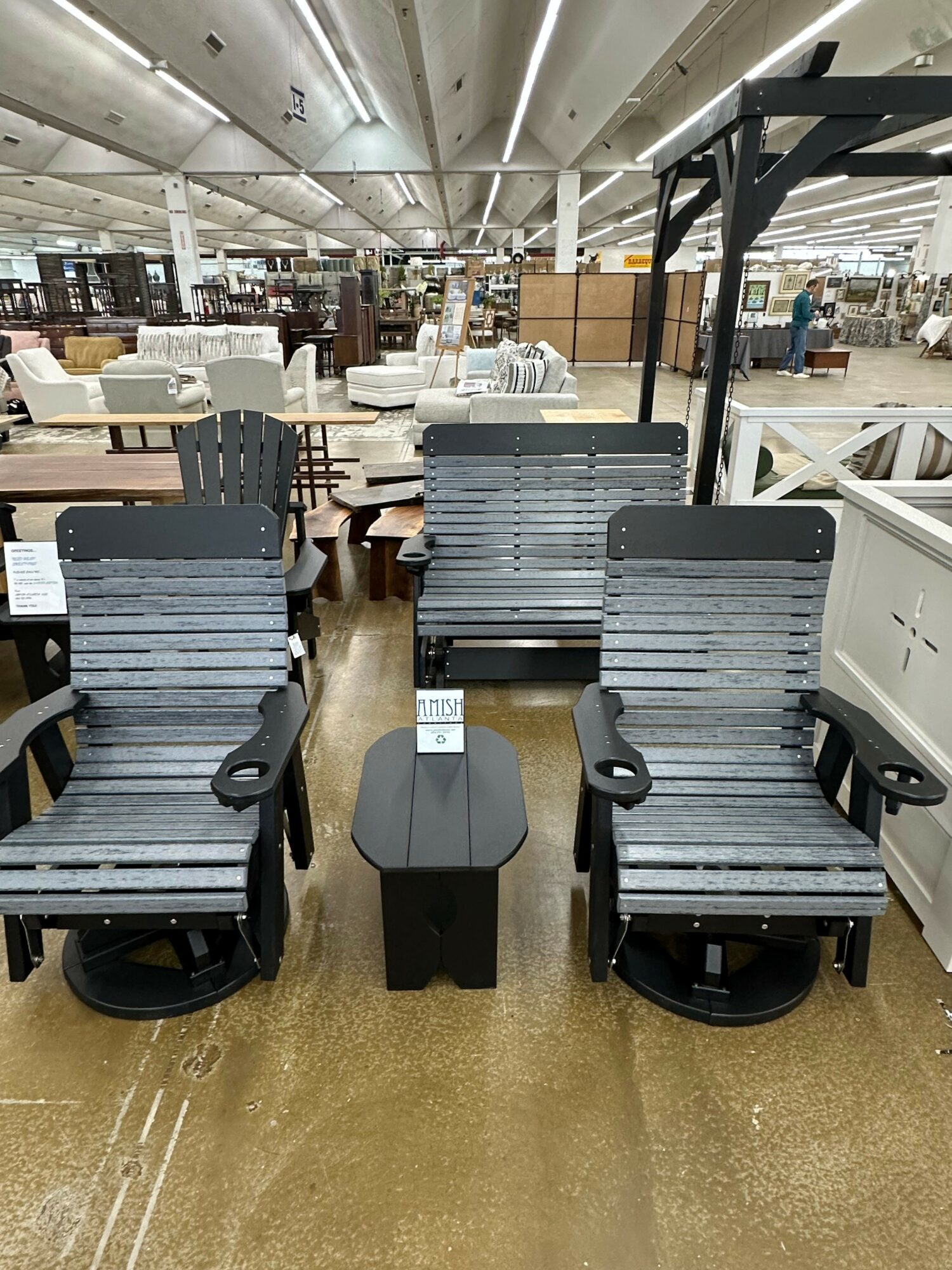 Two black and gray outdoor chairs with armrests and a small black table between them in a furniture store.