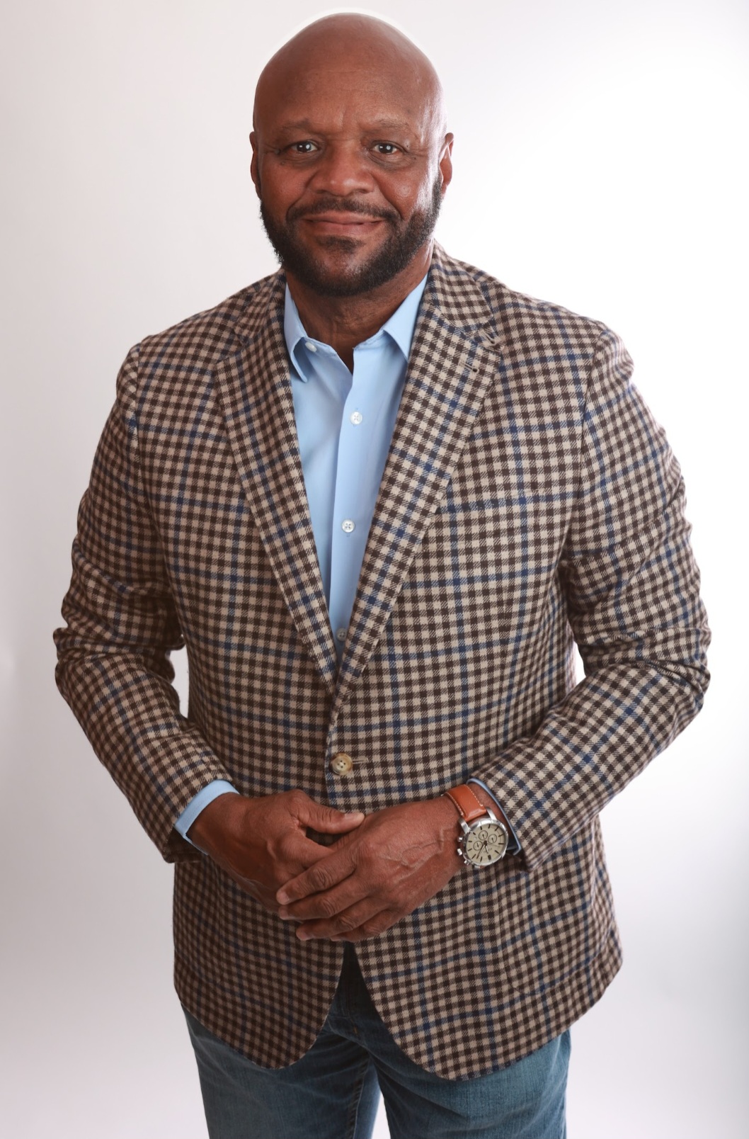 Man with a beard in a checkered blazer and blue shirt, standing against a plain white background.