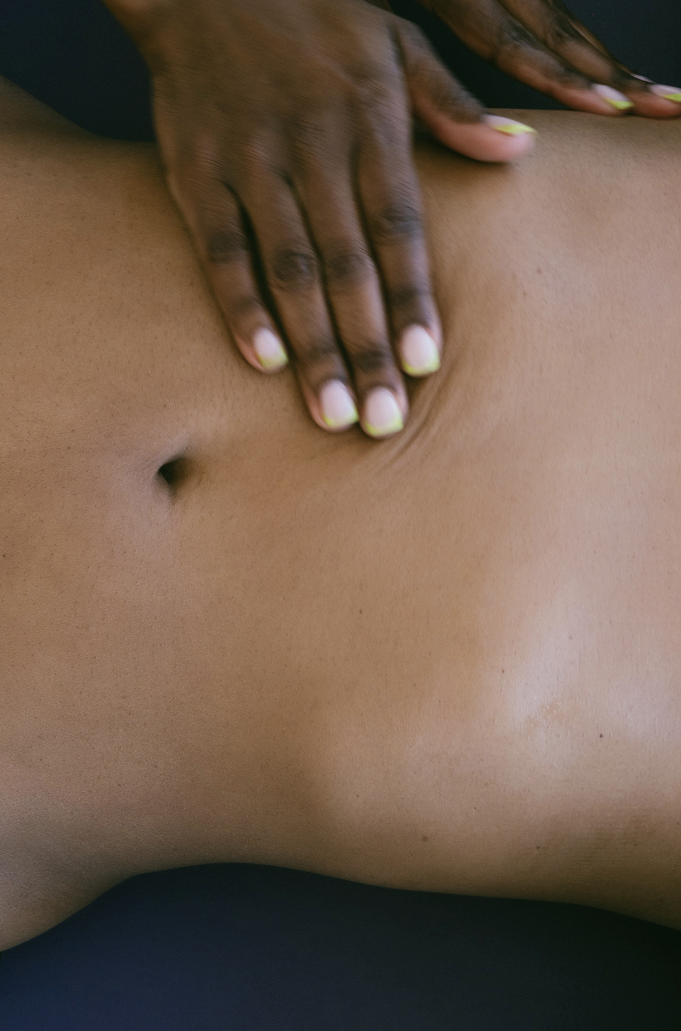 Close-up of a person's hand resting on their bare abdomen, showing skin and belly button.