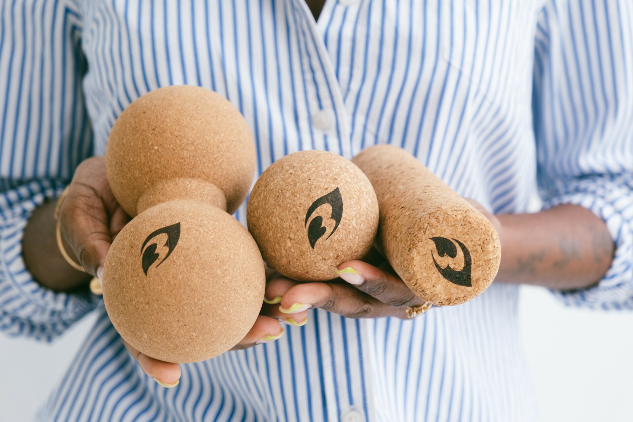 Person holding five round, brown fruits or vegetables with black markings, wearing a blue and white striped shirt.