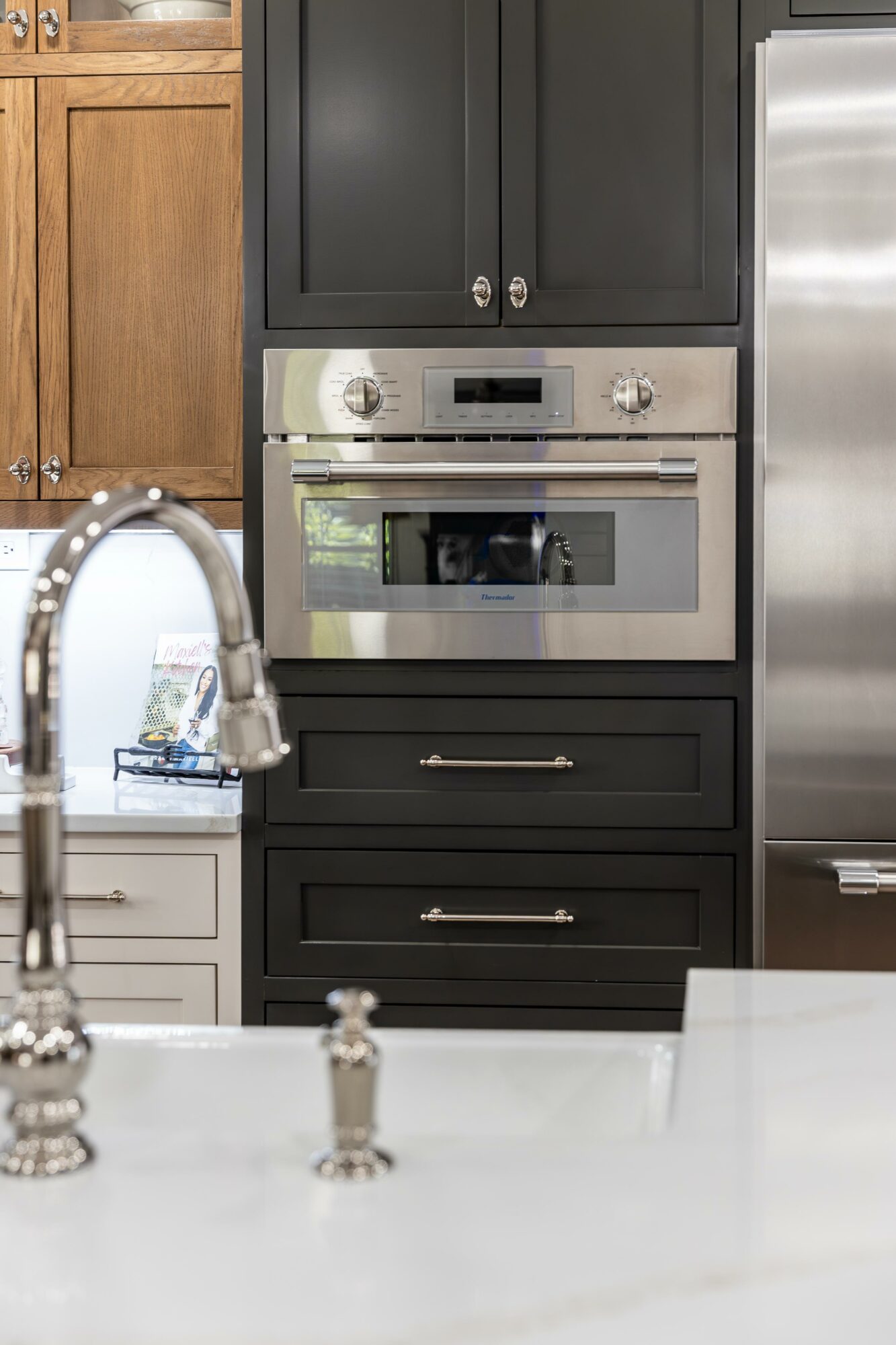 Built-in oven with black cabinetry, stainless steel handle, and control panel, surrounded by kitchen cabinets and a refrigerator.