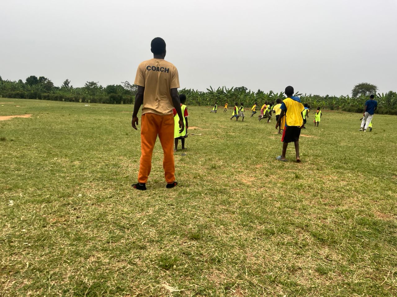 Person standing on grassy field watching a group of children playing soccer in the distance.