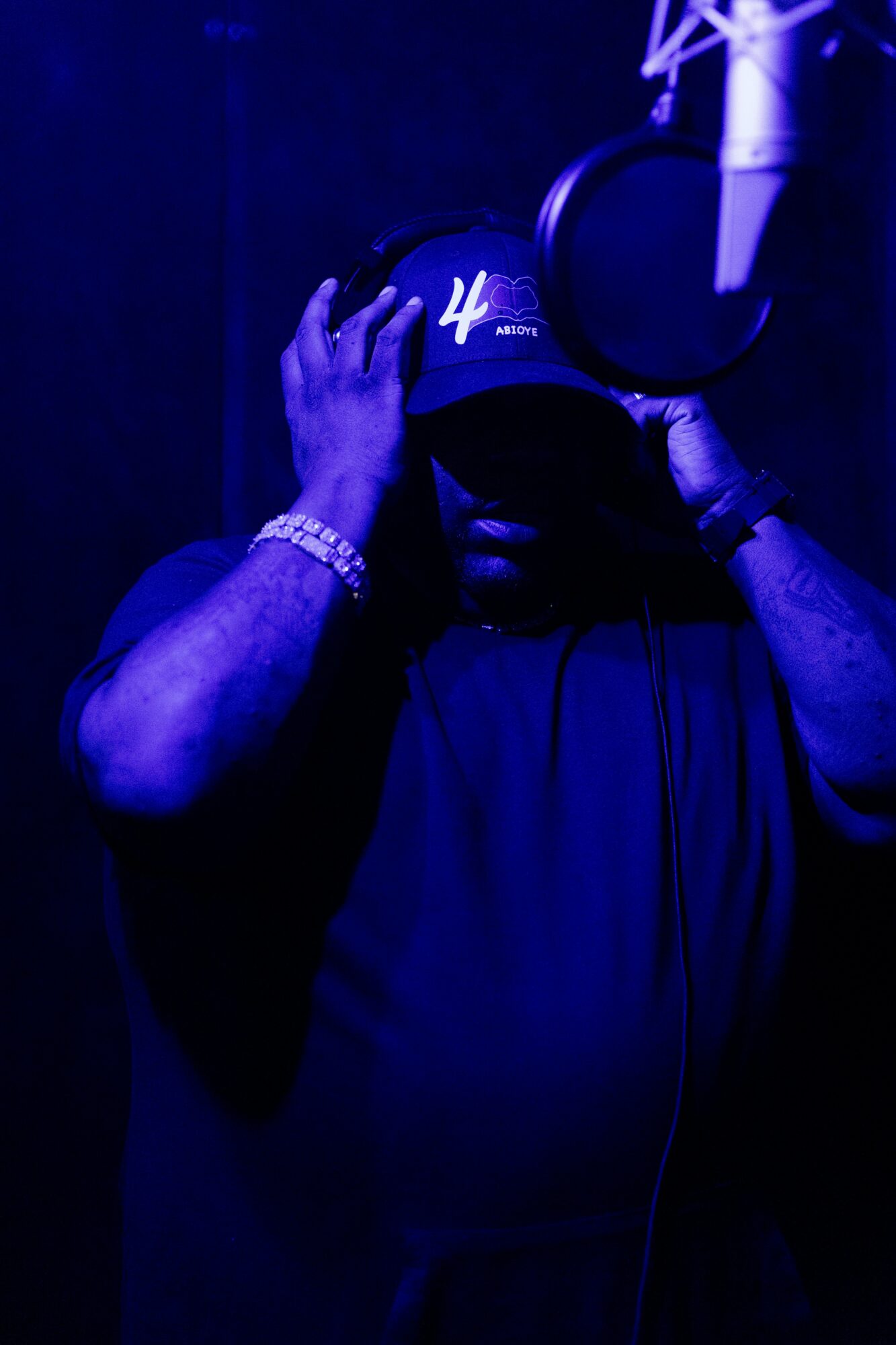 Person wearing a cap and headphones, adjusting the cap in a dark, blue-lit environment.