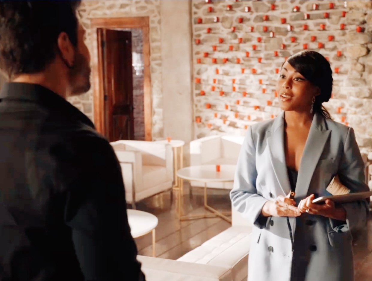 Two people talking in a modern room with brick wall, white furniture, and warm lighting.