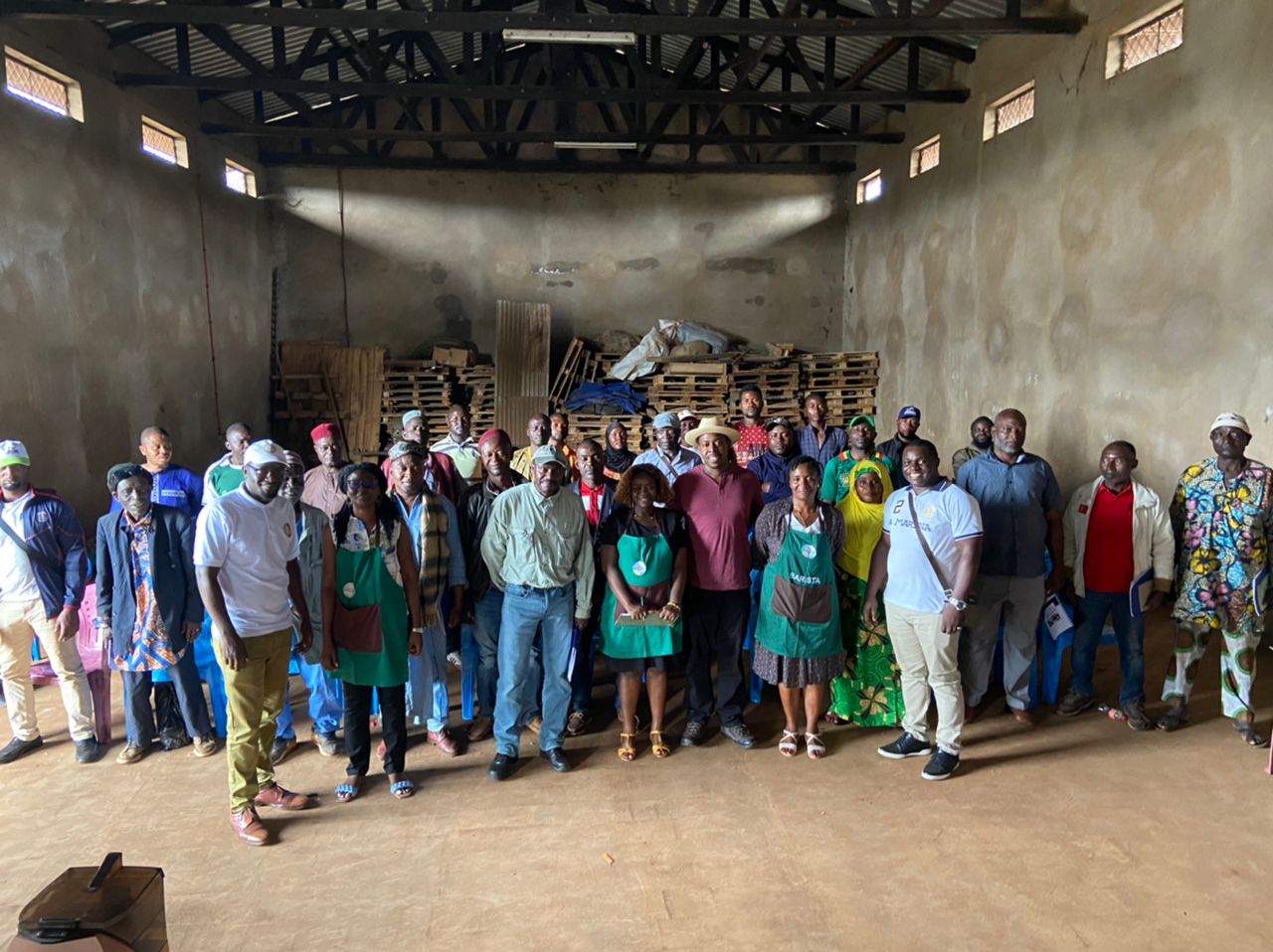 Group of people standing inside a large, unfinished building with high walls and small windows, some wearing masks.