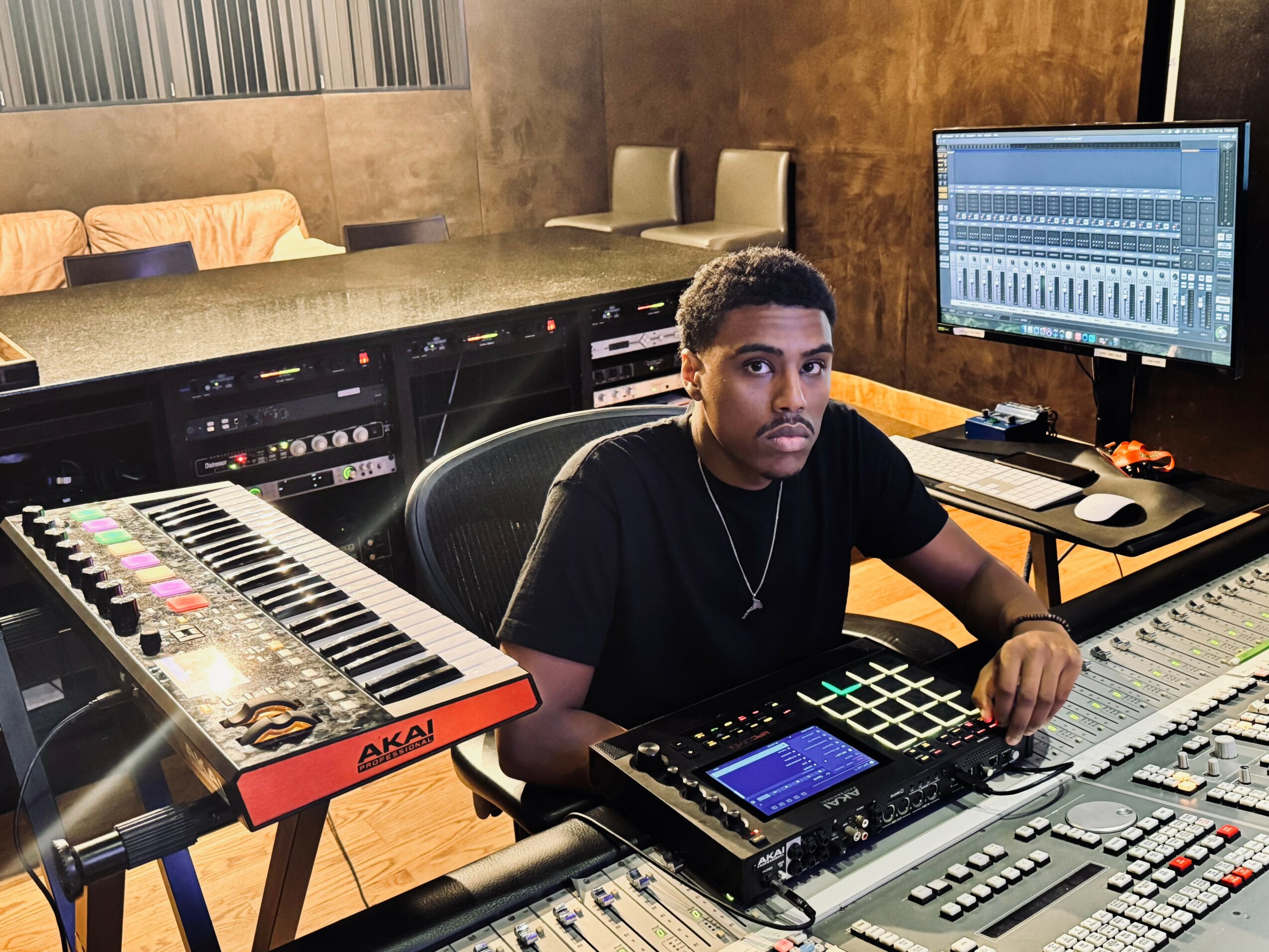 Young man in a music studio with audio equipment, a computer monitor, and a keyboard, sitting at a mixing console.