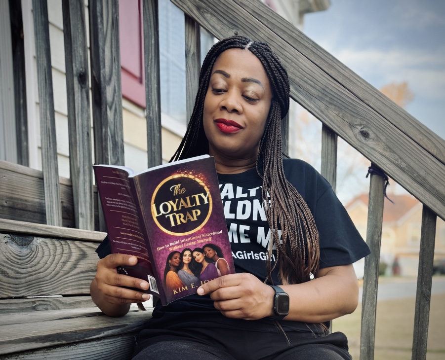 Woman sitting on stairs reading a book titled 'Loyalty Trap' outdoors.
