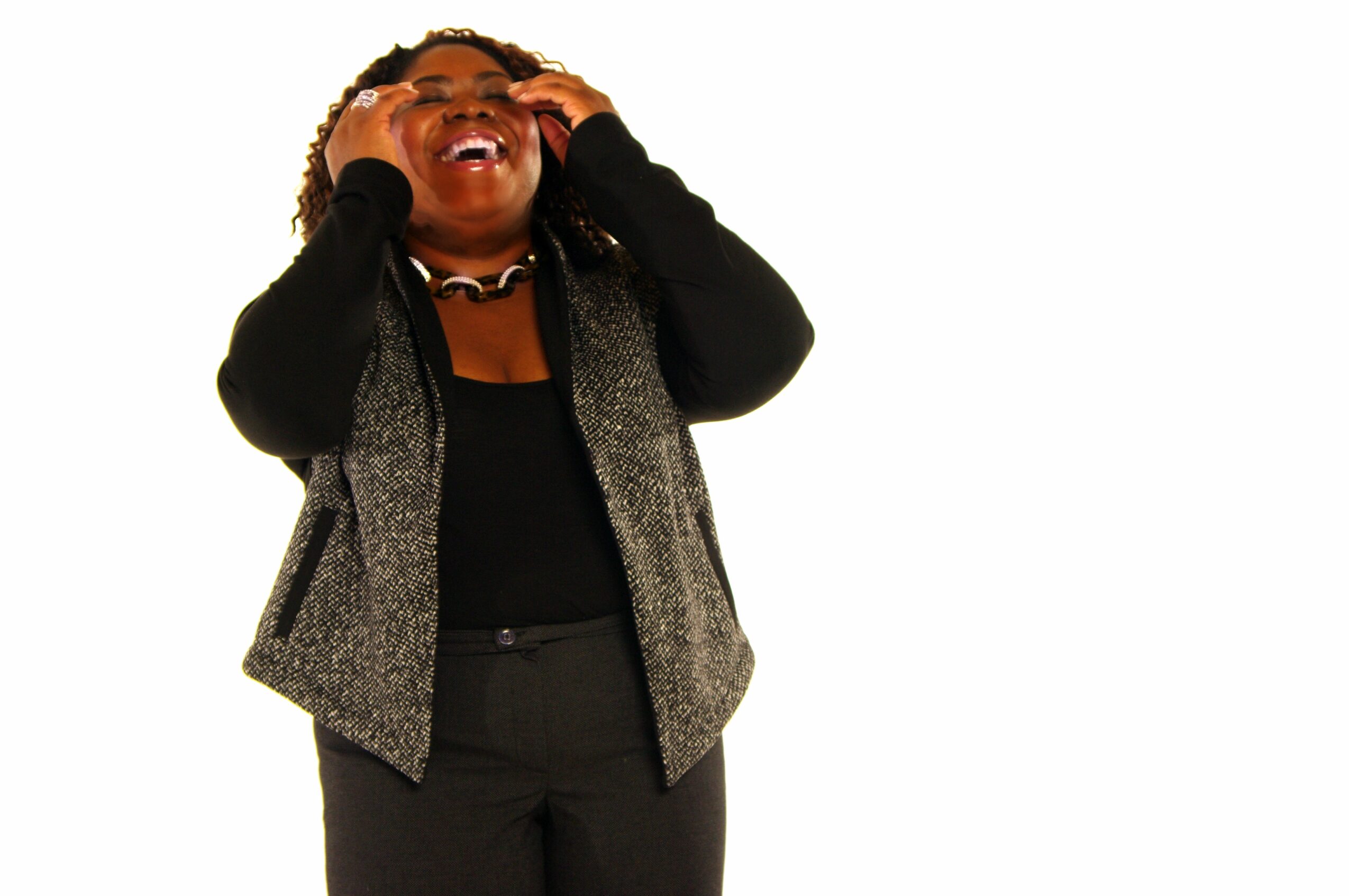 Person laughing with hands on head, wearing black and gray clothing, against a white background.