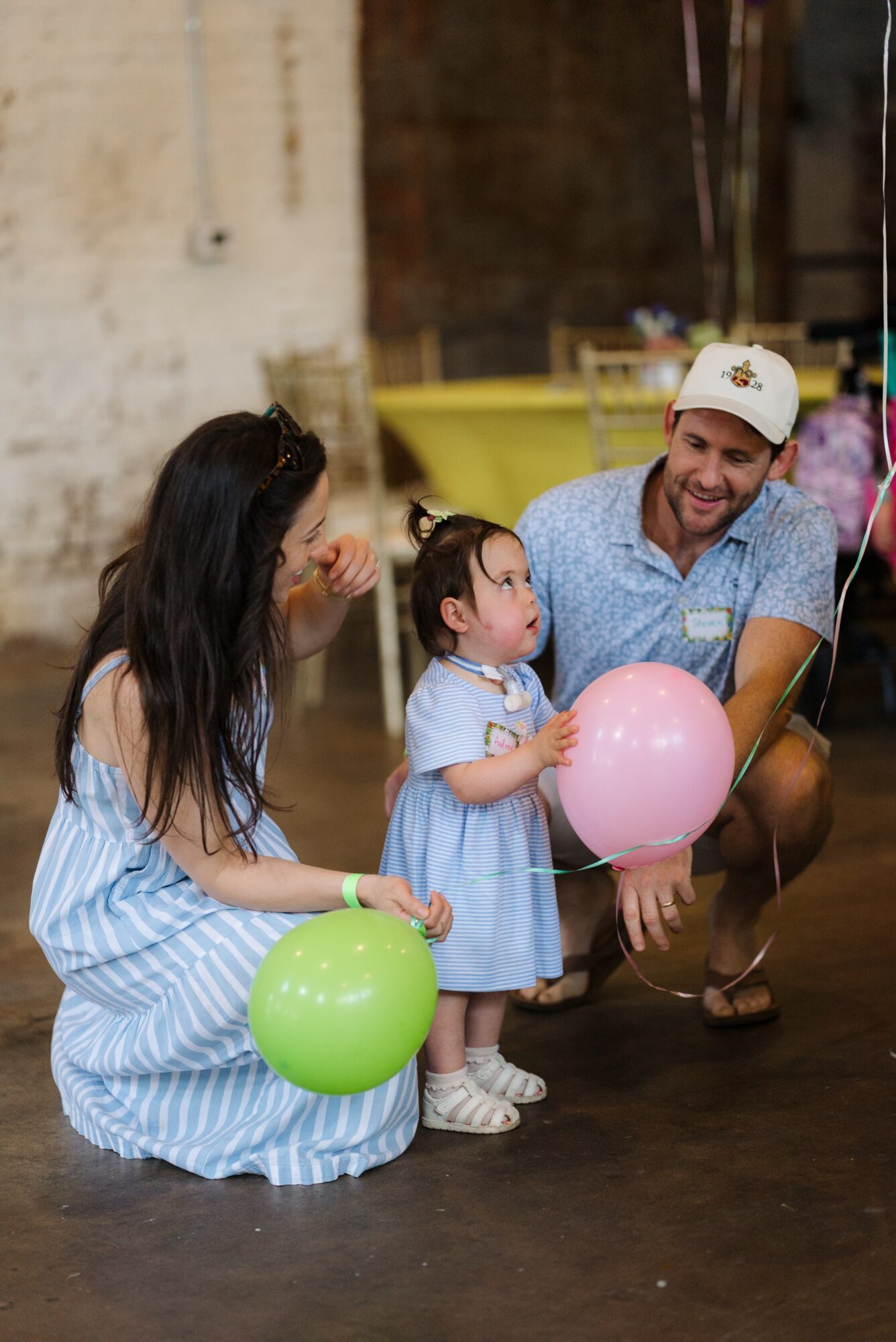 Family with two children holding balloons, indoors with balloons and decorations in background.