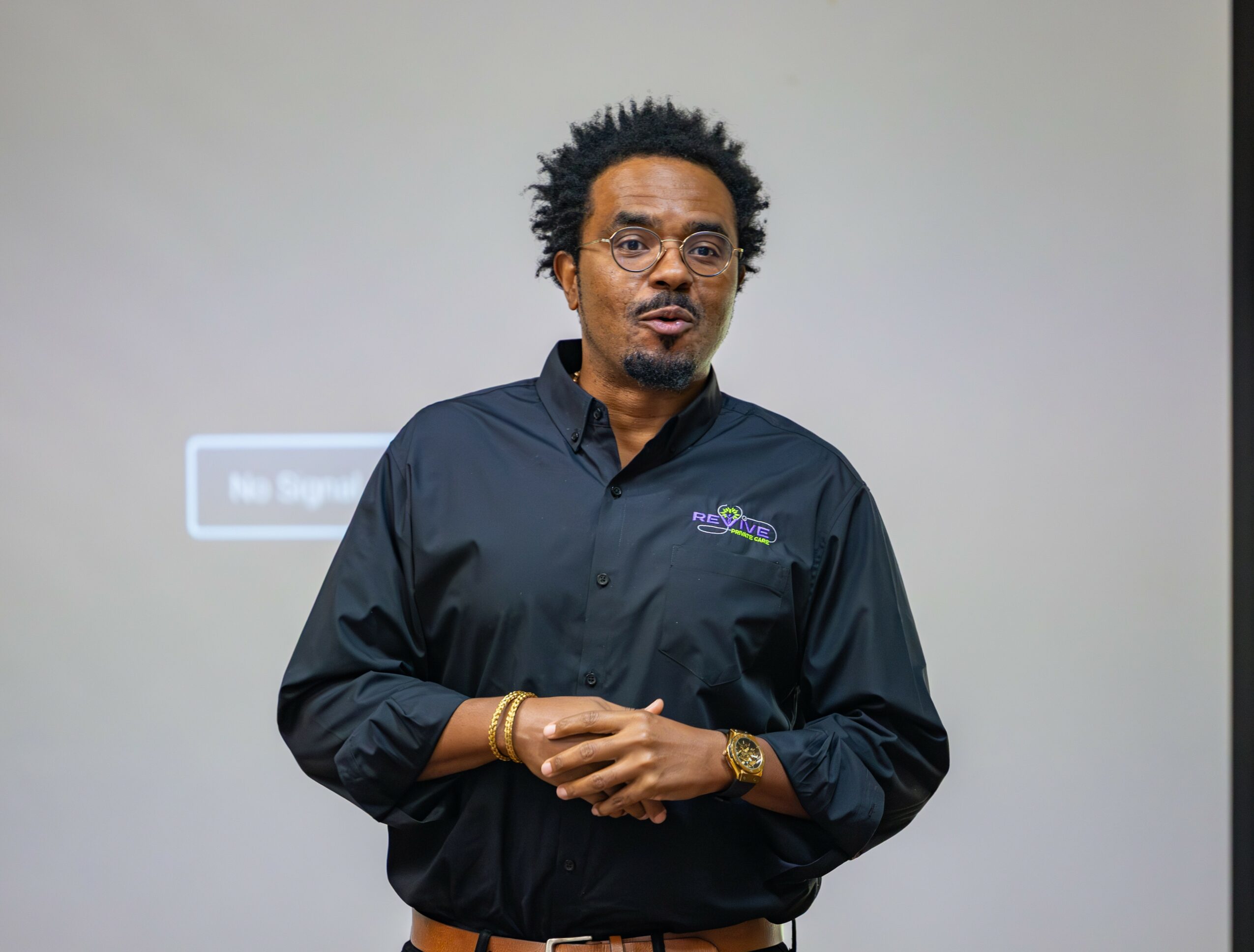 Man with glasses and curly hair wearing a black shirt, standing in front of a plain background.