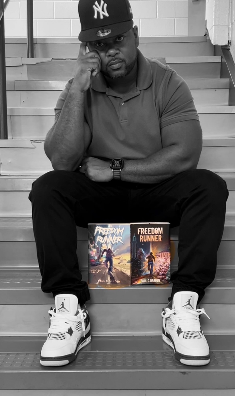 Man sitting on stairs with two books in front, wearing a cap, polo shirt, sneakers, and a watch.