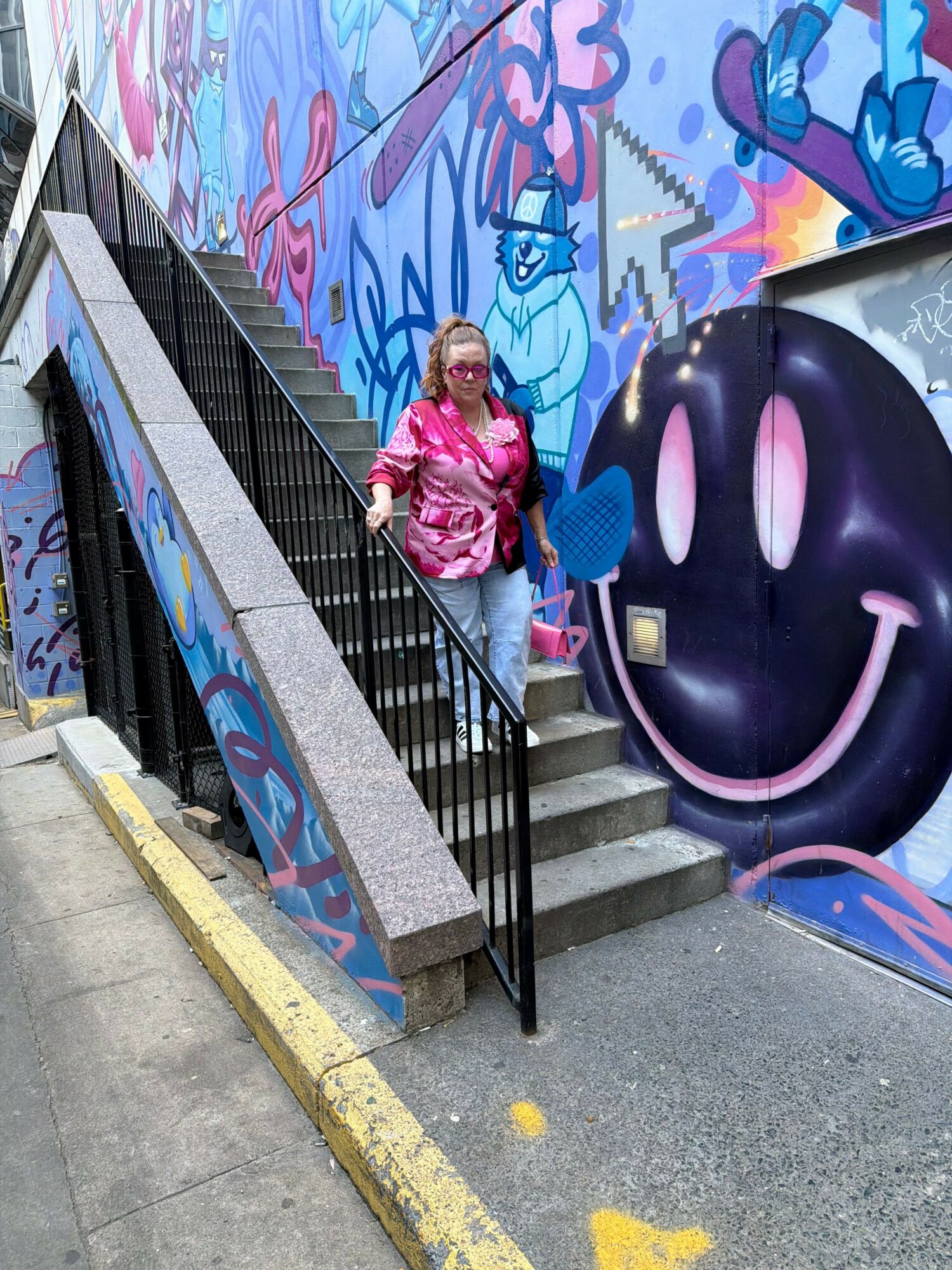 Person in pink jacket walking up stairs next to graffiti-covered wall with large black and pink mural.