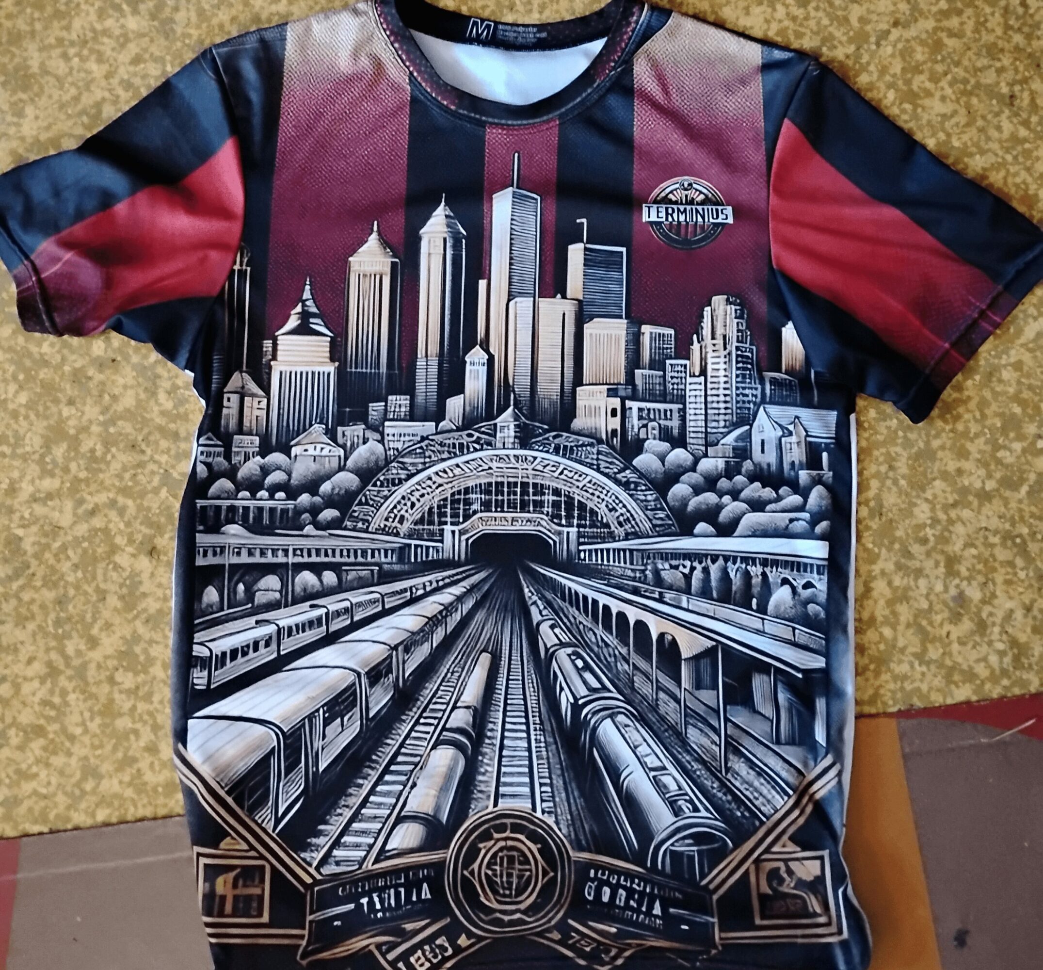 T-shirt with a cityscape and train tracks design, featuring skyscrapers and a bridge, in black, white, and red colors.