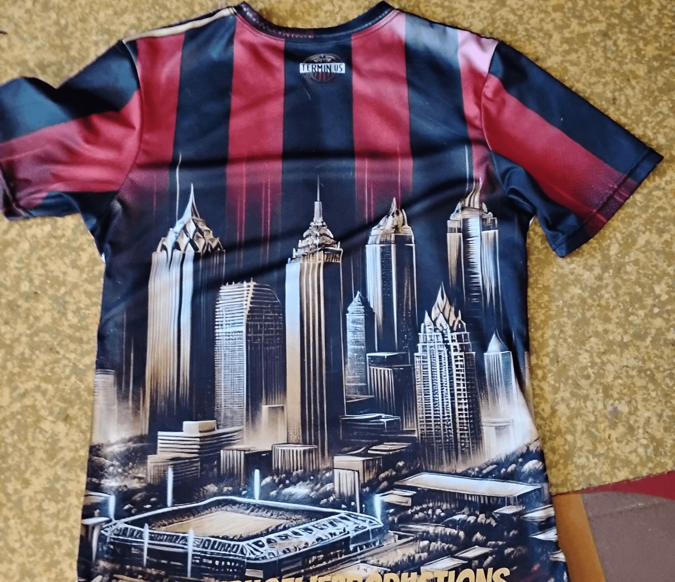 T-shirt with a city skyline and tall buildings printed on it, featuring a red and black striped pattern on the shoulders.