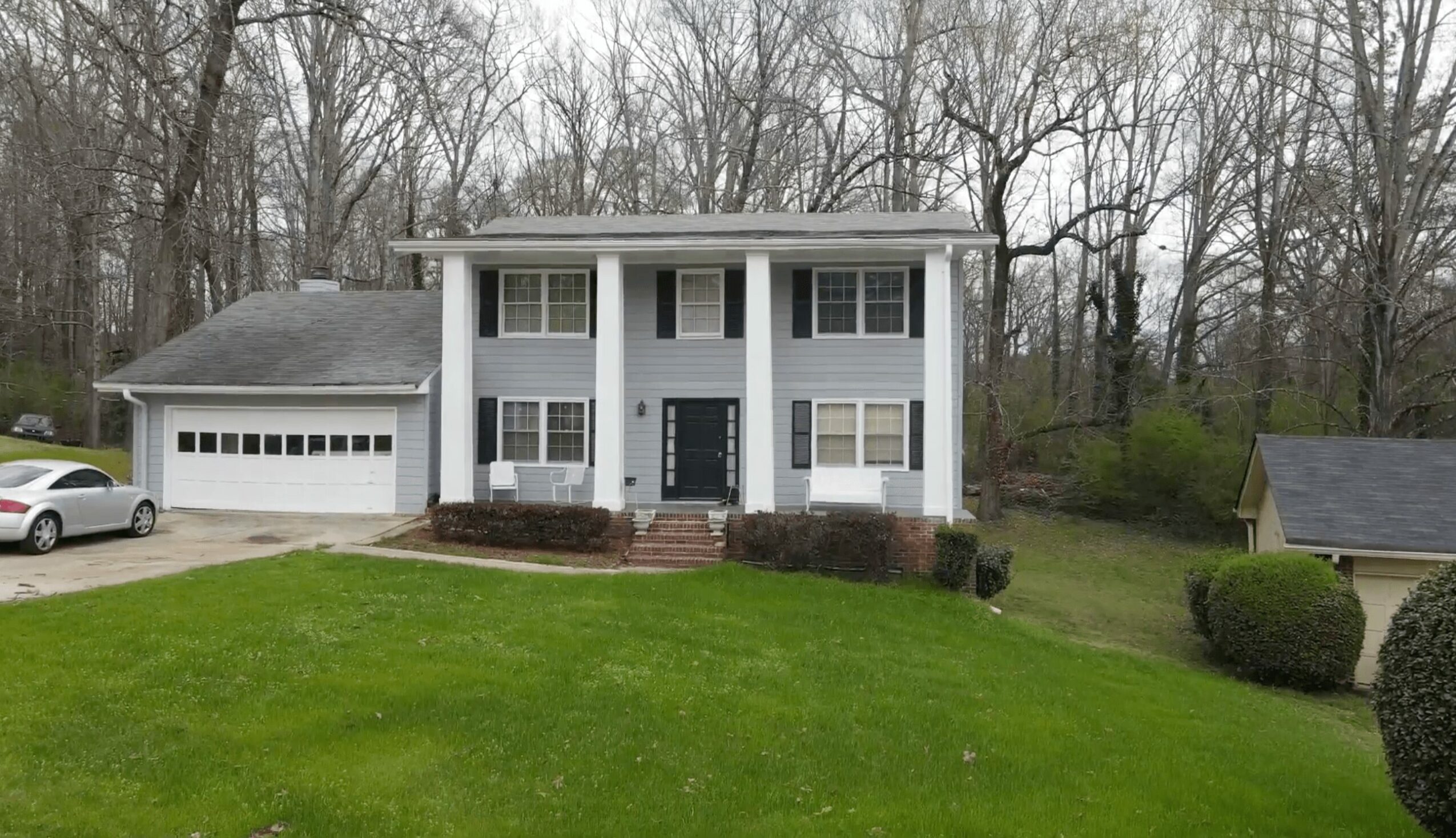 Two-story house with white exterior, front steps, and a garage, surrounded by trees and a grassy lawn.