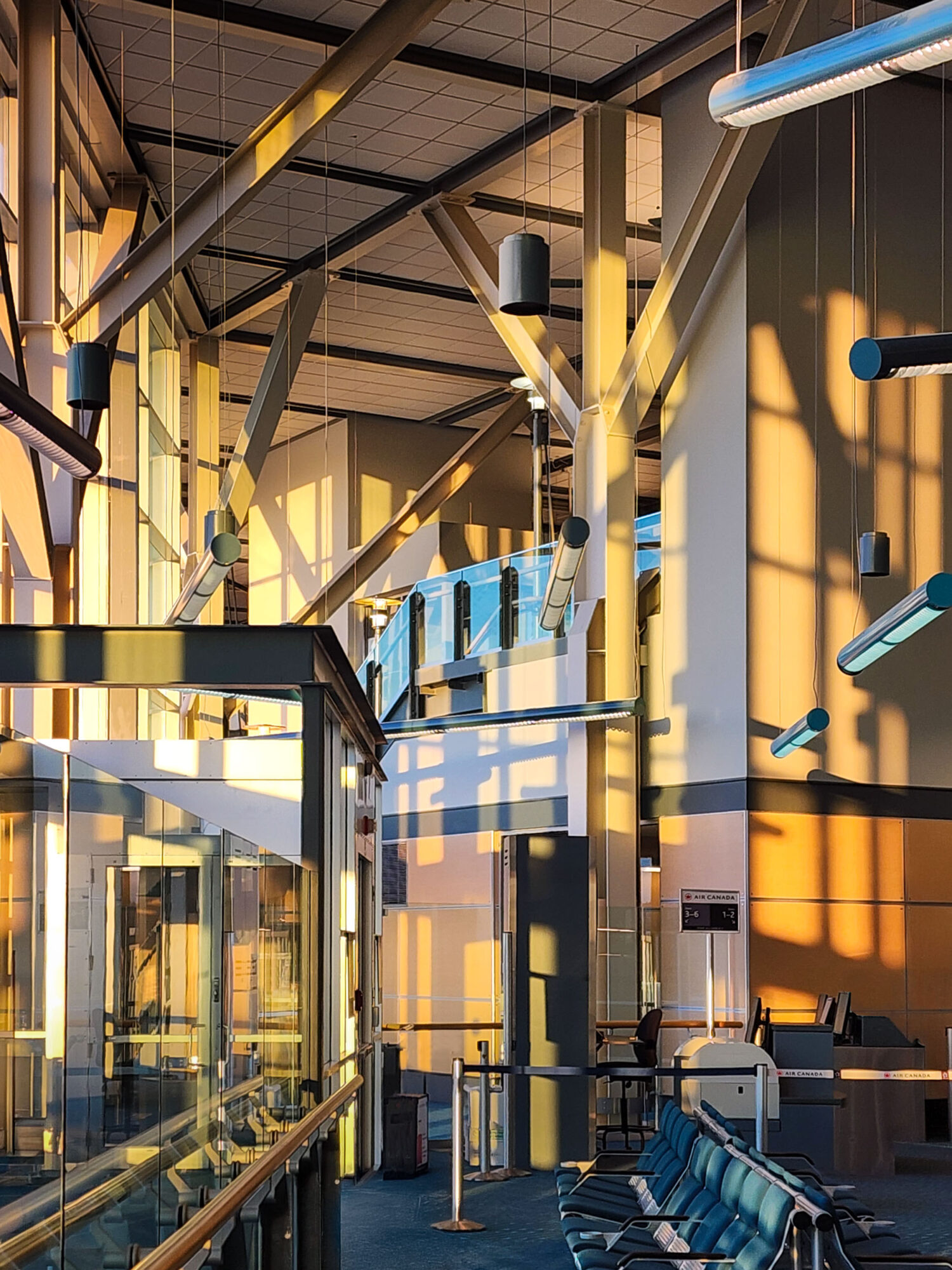 Interior of a modern building with yellow structural elements, glass walls, and colorful lighting fixtures, with sunlight casting shadows.