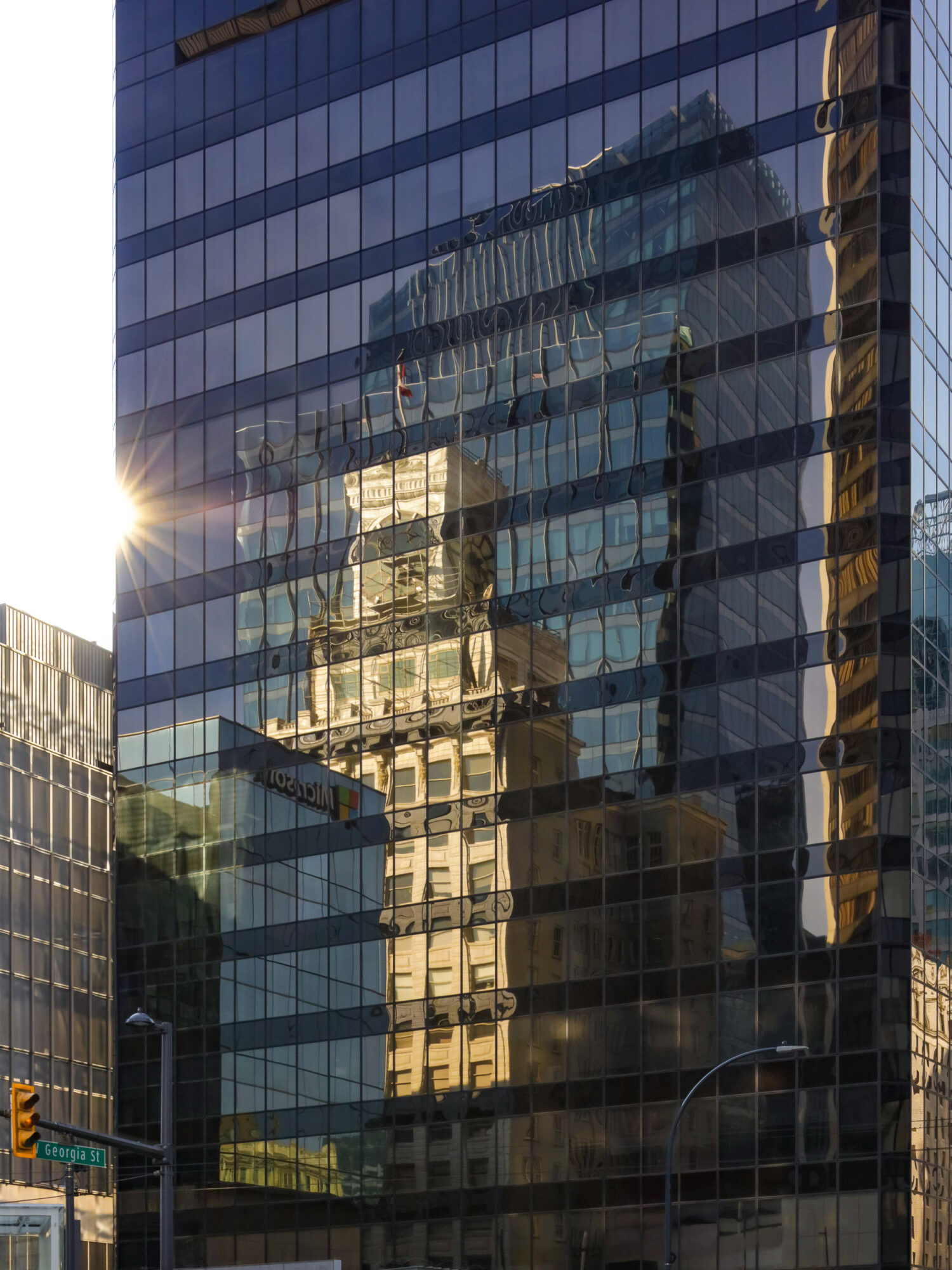 Reflected building and sky in a glass skyscraper with grid pattern, sunlight on left side, urban scene.