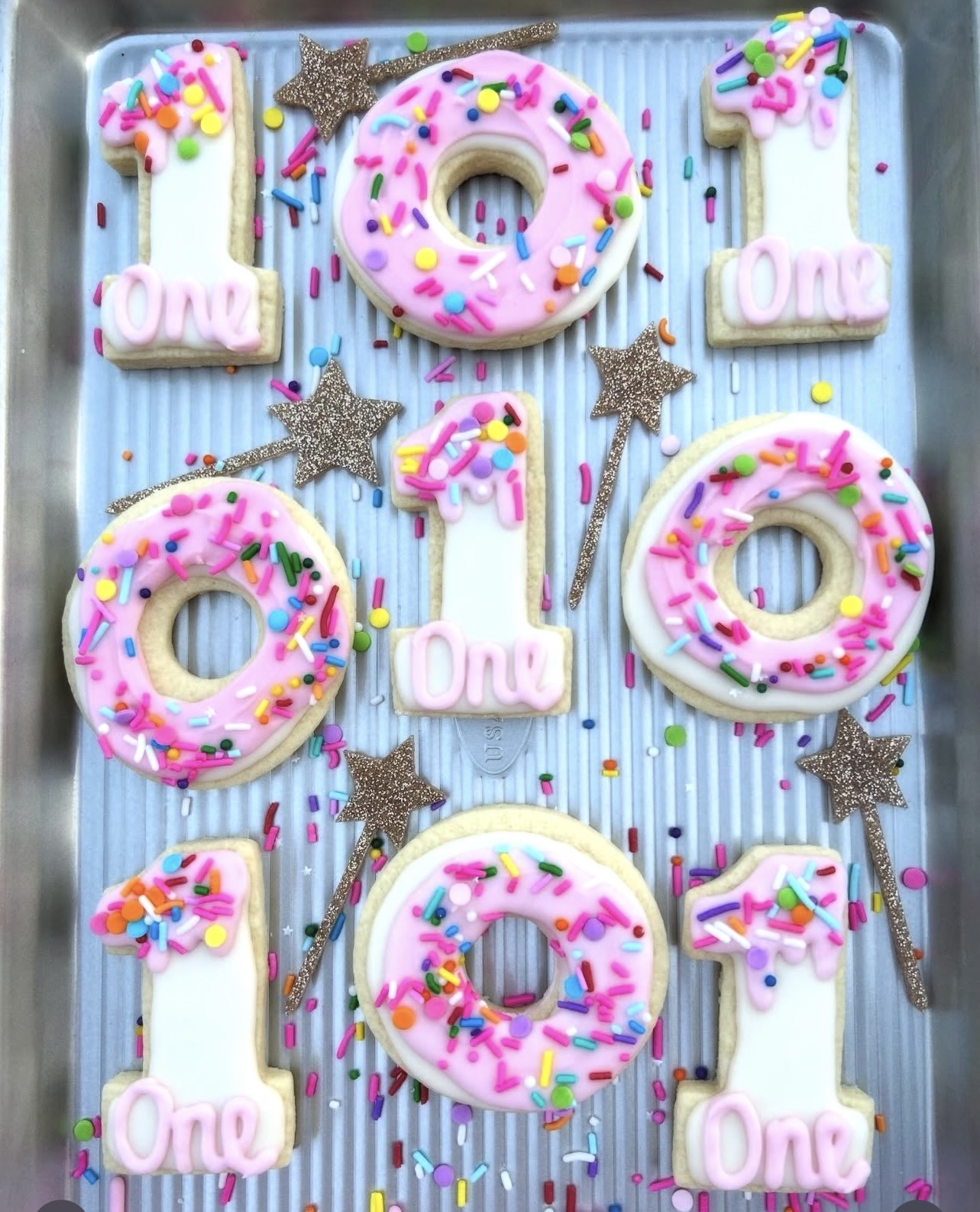 Decorative birthday cake with pink donuts, star-shaped toppers, and colorful sprinkles on a striped blue background.