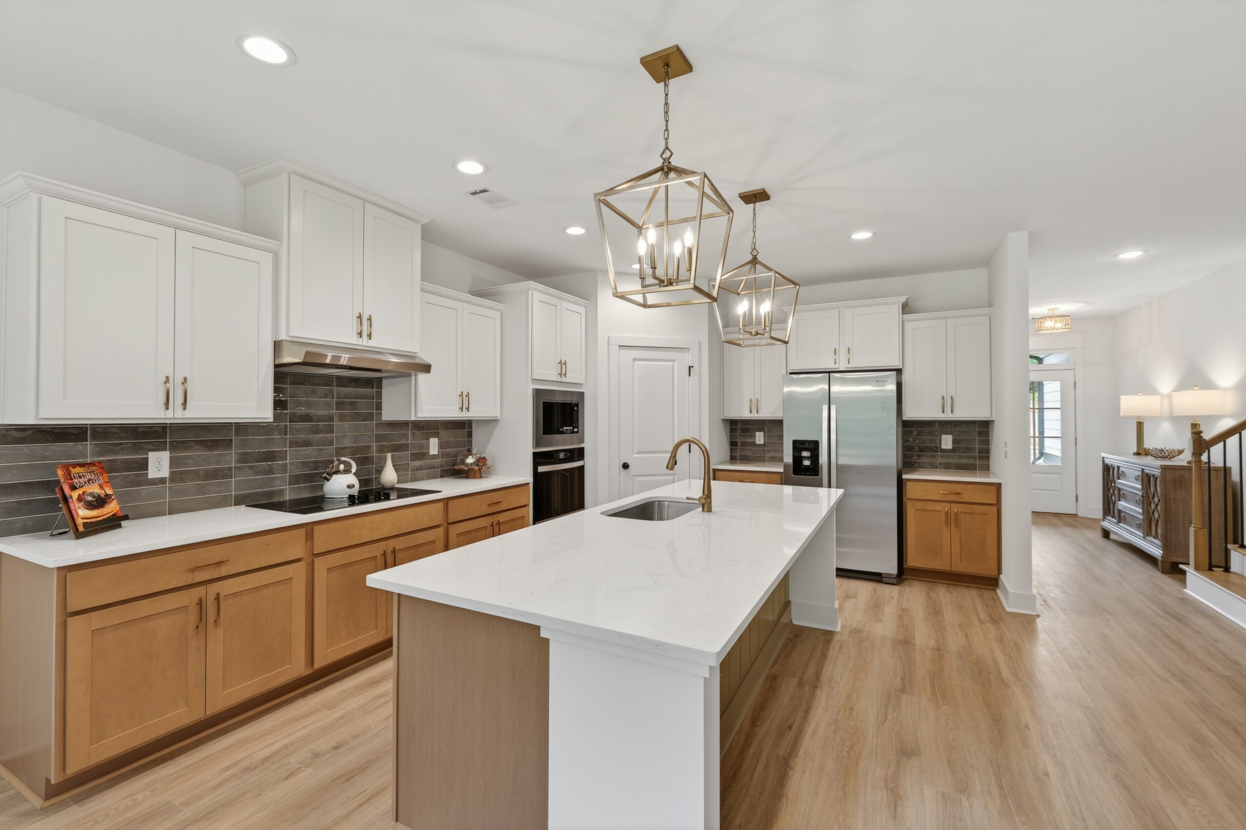 Modern kitchen with white cabinets, a large island, pendant lights, and stainless steel appliances, with hardwood floors and a bright open layout.