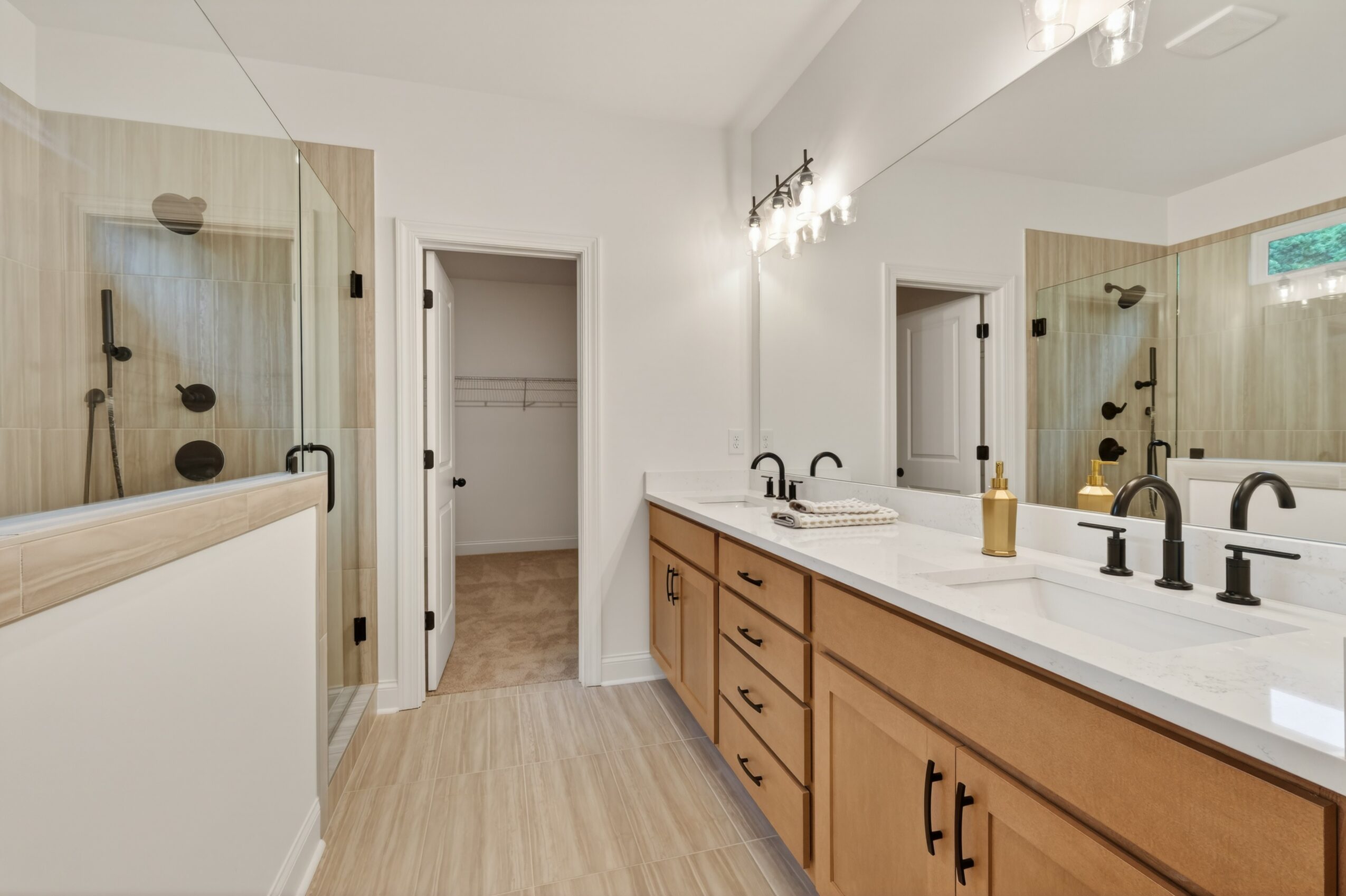 Bathroom with double vanity, large mirror, and walk-in shower with glass door, wood accents, and neutral colors.