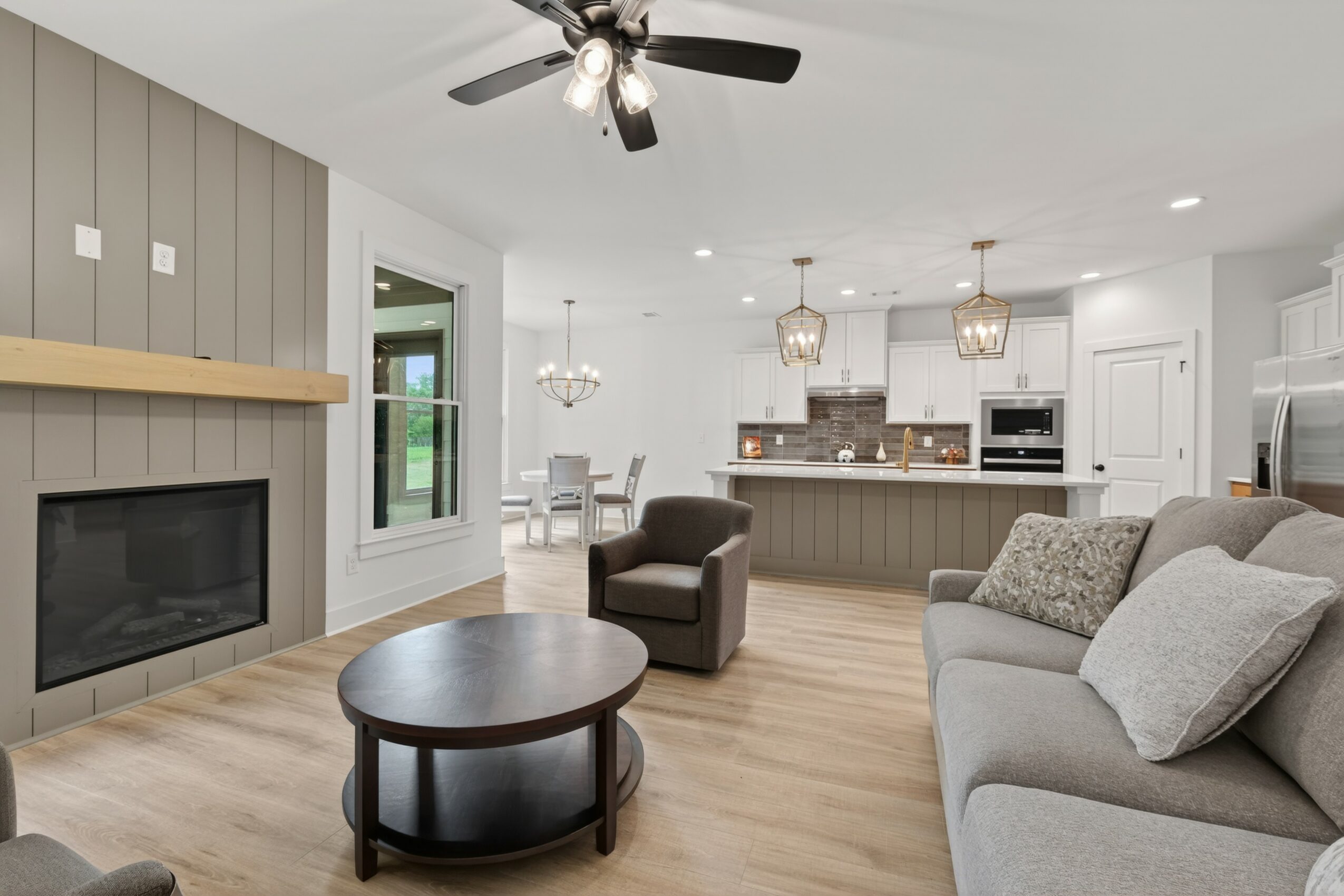 Living room with fireplace, gray sofa, armchair, round coffee table, and open kitchen with island and dining area, bright and spacious.