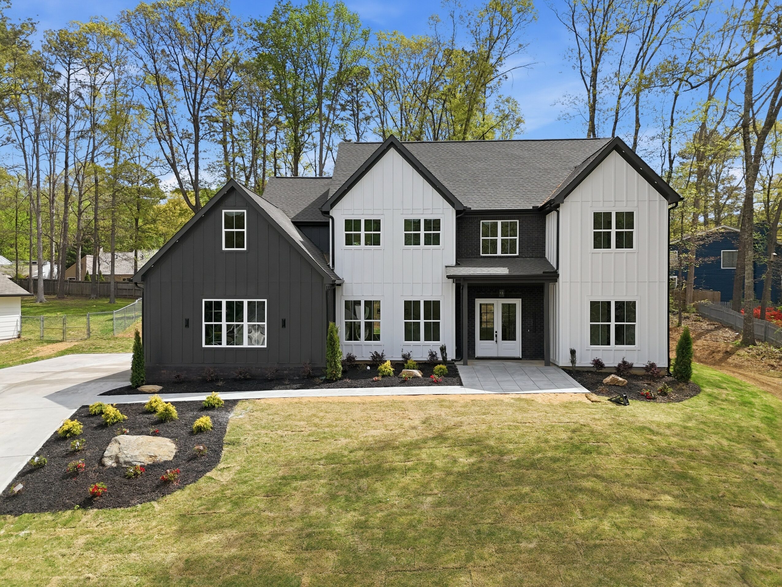 Modern two-story house with black and white exterior, front yard with landscaping, and a paved walkway leading to the entrance.