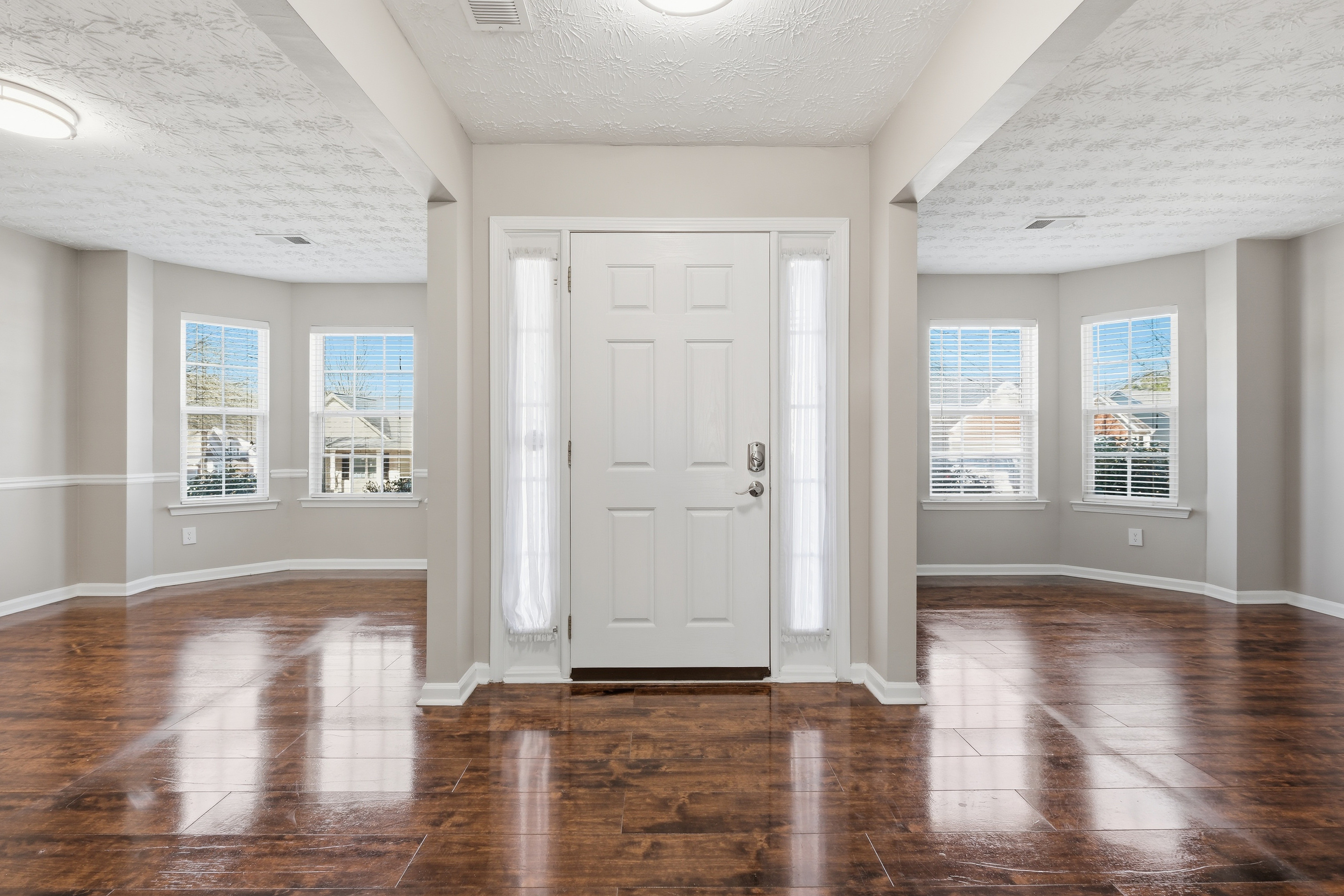 Front door with windows on each side, leading into a bright room with hardwood floors and multiple windows.