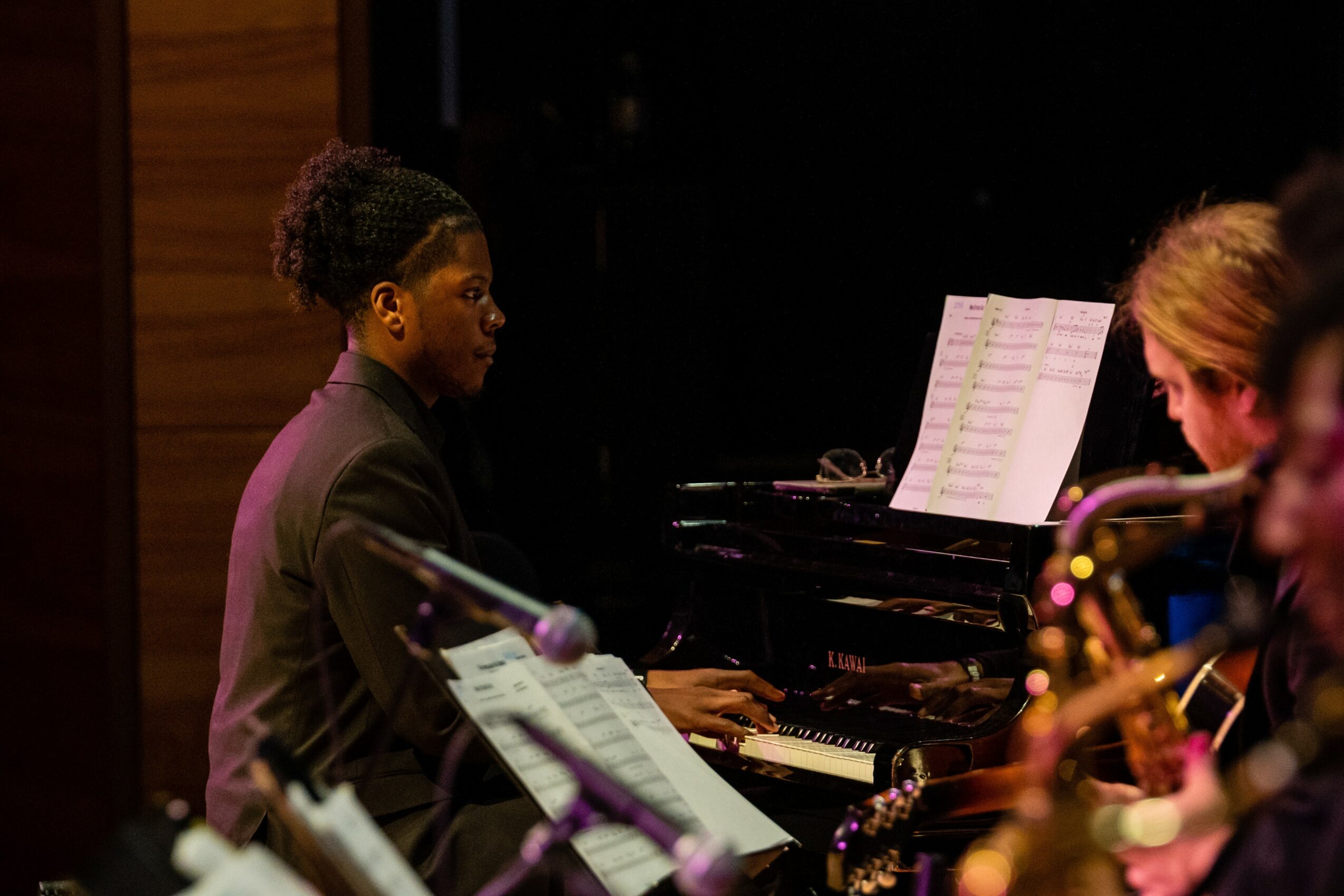 Two women playing musical instruments, one on piano and the other on saxophone, in a dimly lit setting.