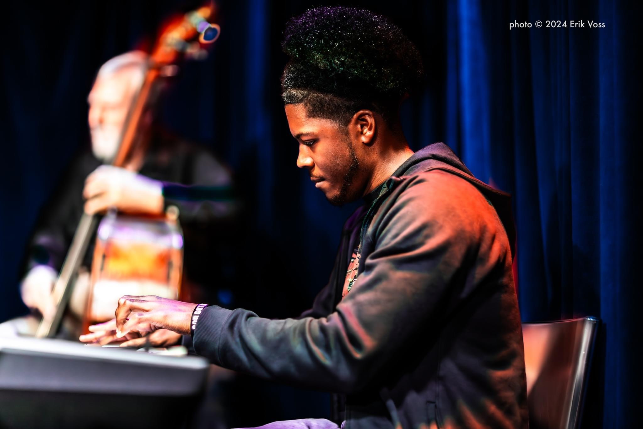 Young man playing piano on stage with a dark blue curtain background.
