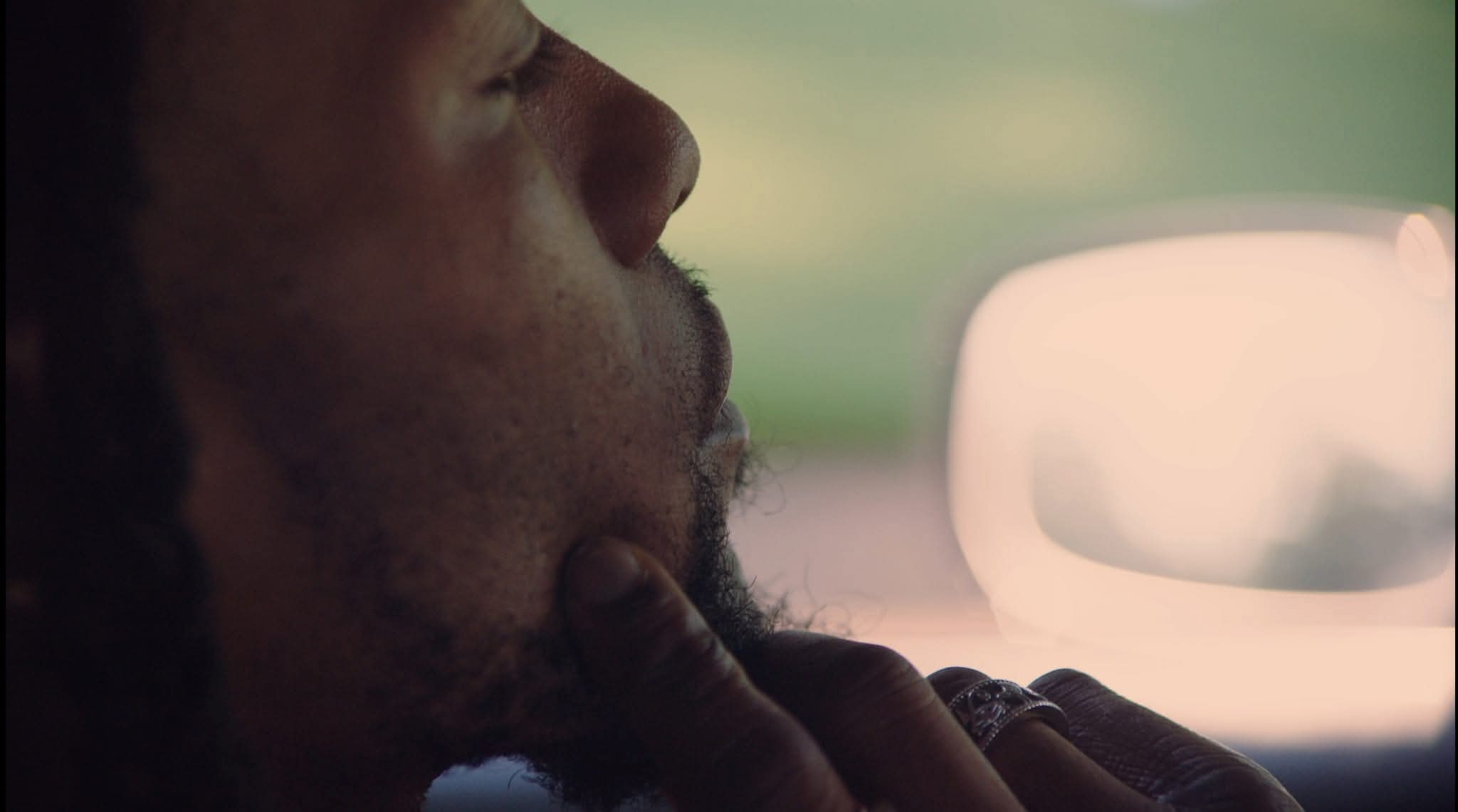Close-up of a person with a beard, resting their chin on their hand inside a vehicle.