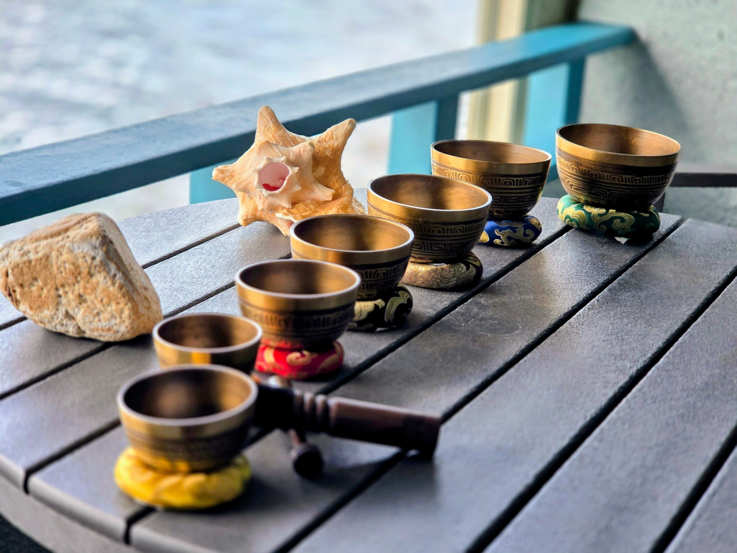 Six black cups with gold rims arranged on a dark wooden table, with a star-shaped cookie, a rock, and a small red object nearby.