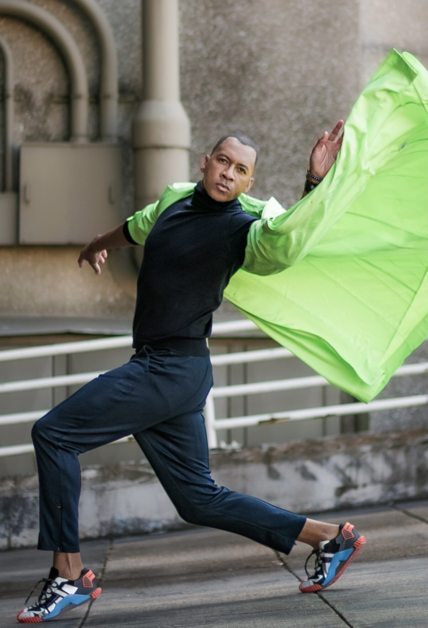 Person in athletic clothing holding a bright green flag, mid-movement on a city street, with a stone building background.