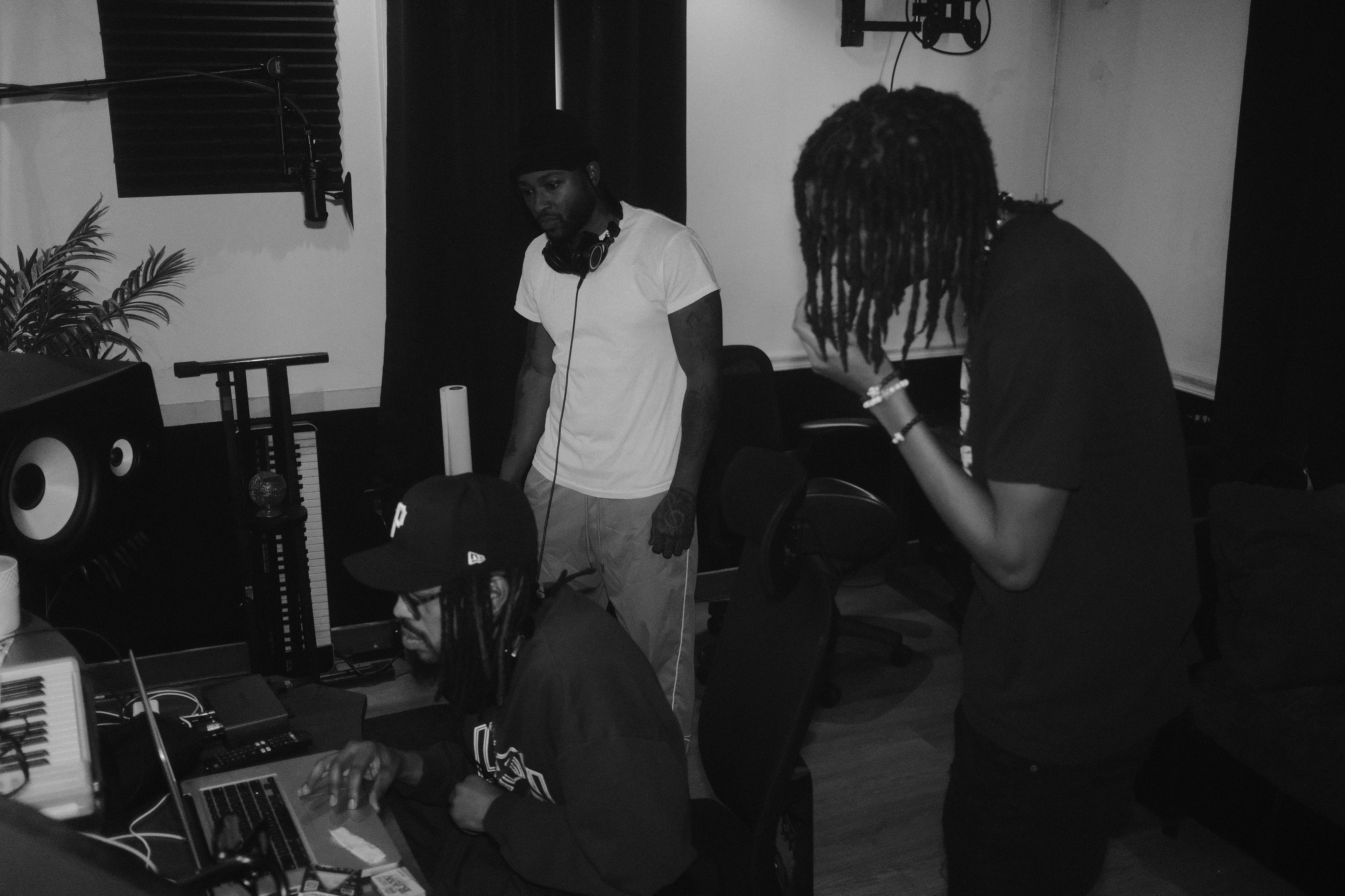 Two people in a music studio, one sitting at a mixing console and the other standing, both focused on their tasks.