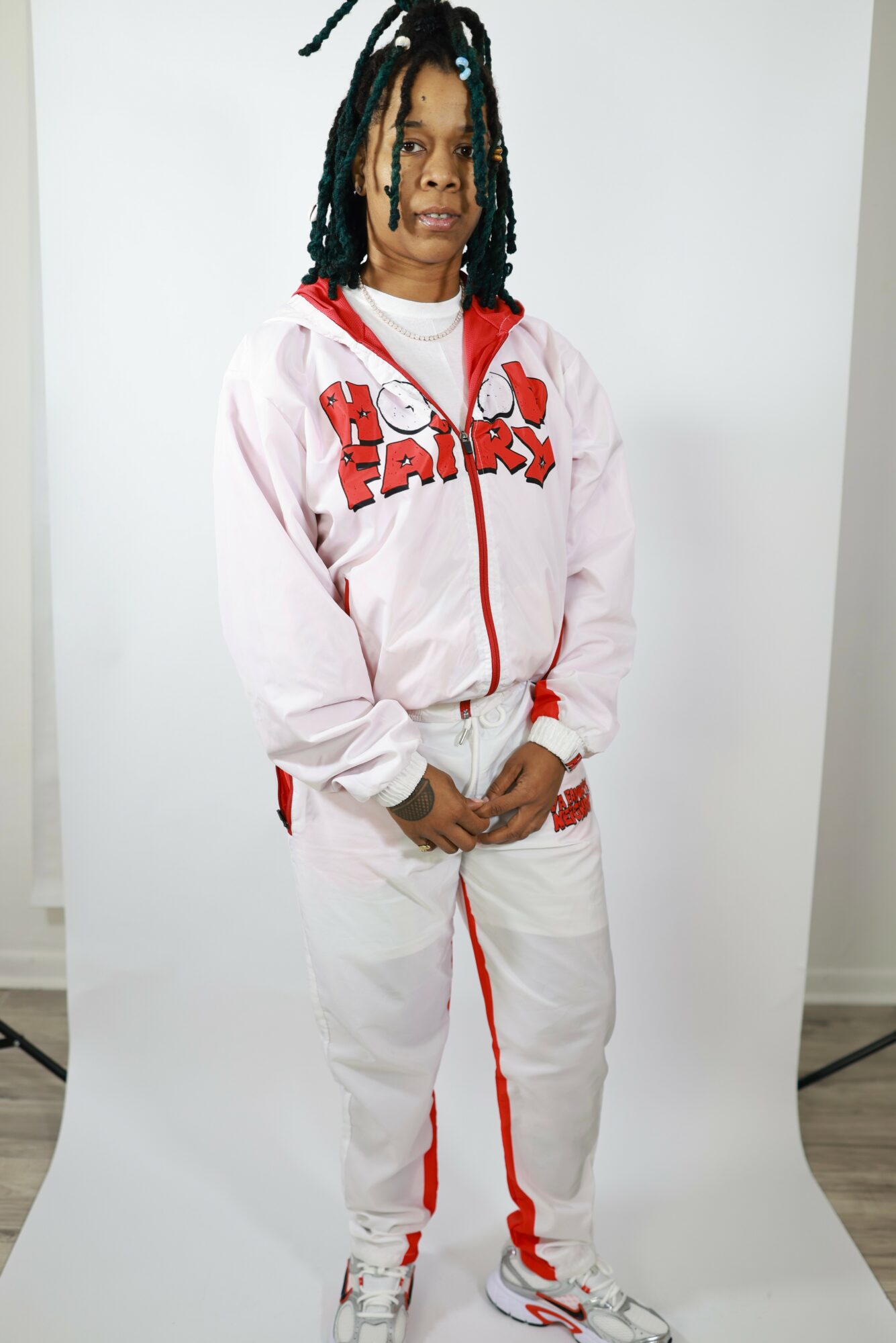 Young person with dreadlocks wearing a pink and white tracksuit, standing against a plain background.