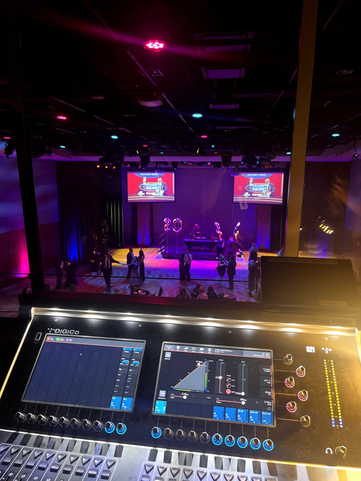 Stage with performers and two screens, colorful lighting, and a control panel in the foreground, 20 words.