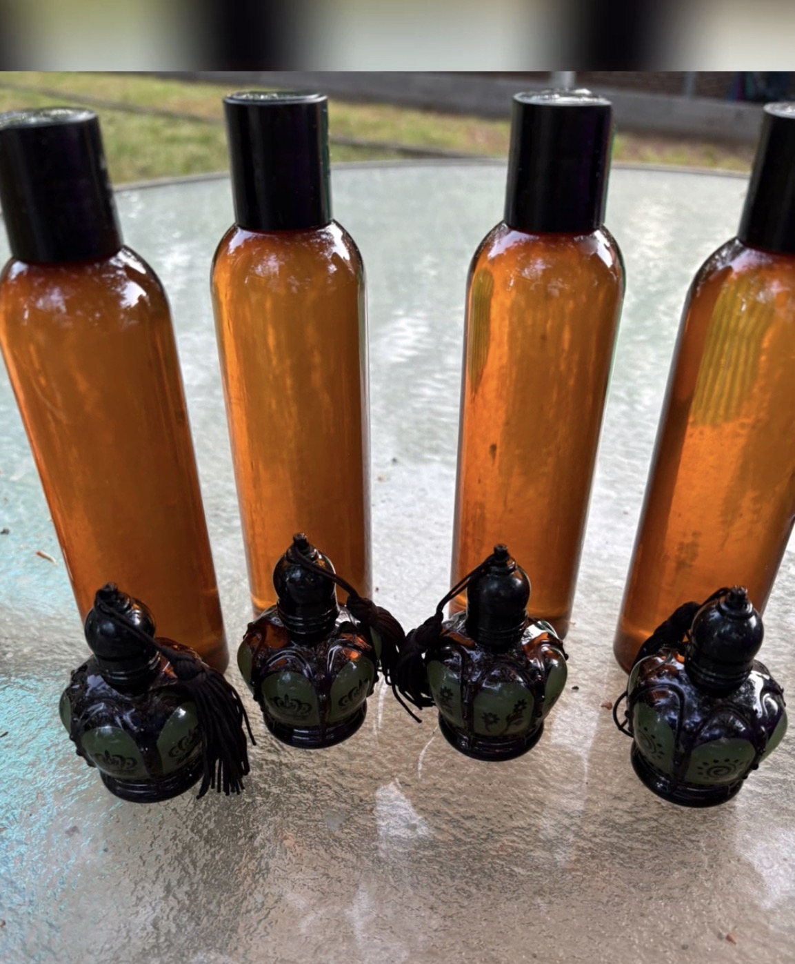 Four amber bottles with black caps and four small black figurines with wings on a reflective surface outdoors.