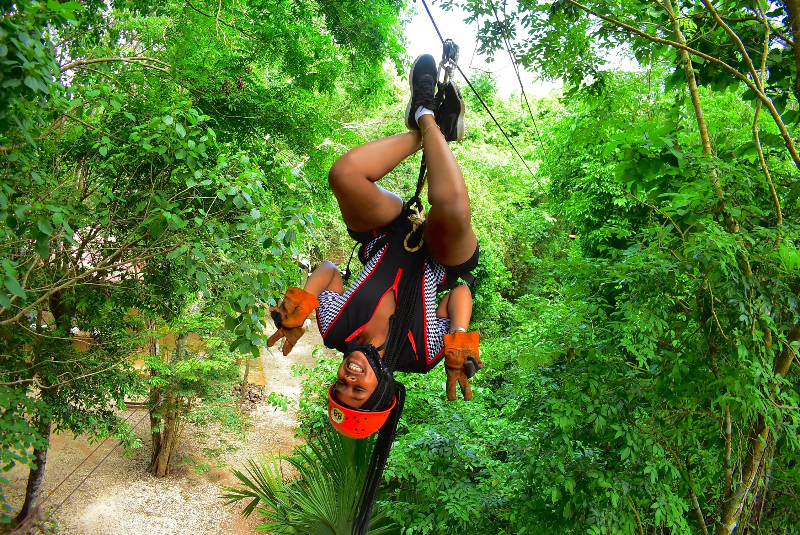 Person hanging upside down from a tree in a forest, wearing safety gear and helmet.