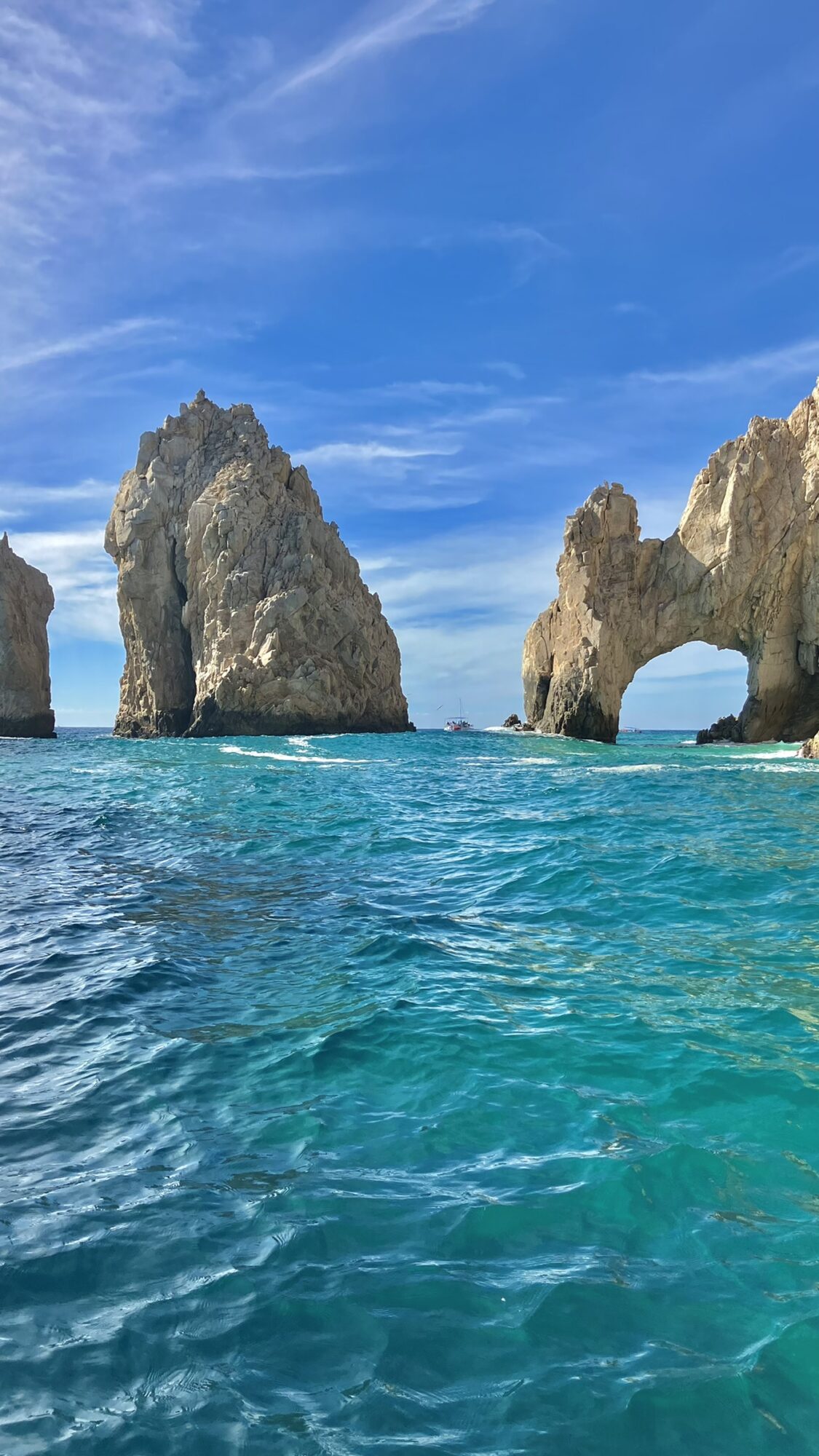Sea with large rock formations and a blue sky with clouds, water appears turquoise and calm.