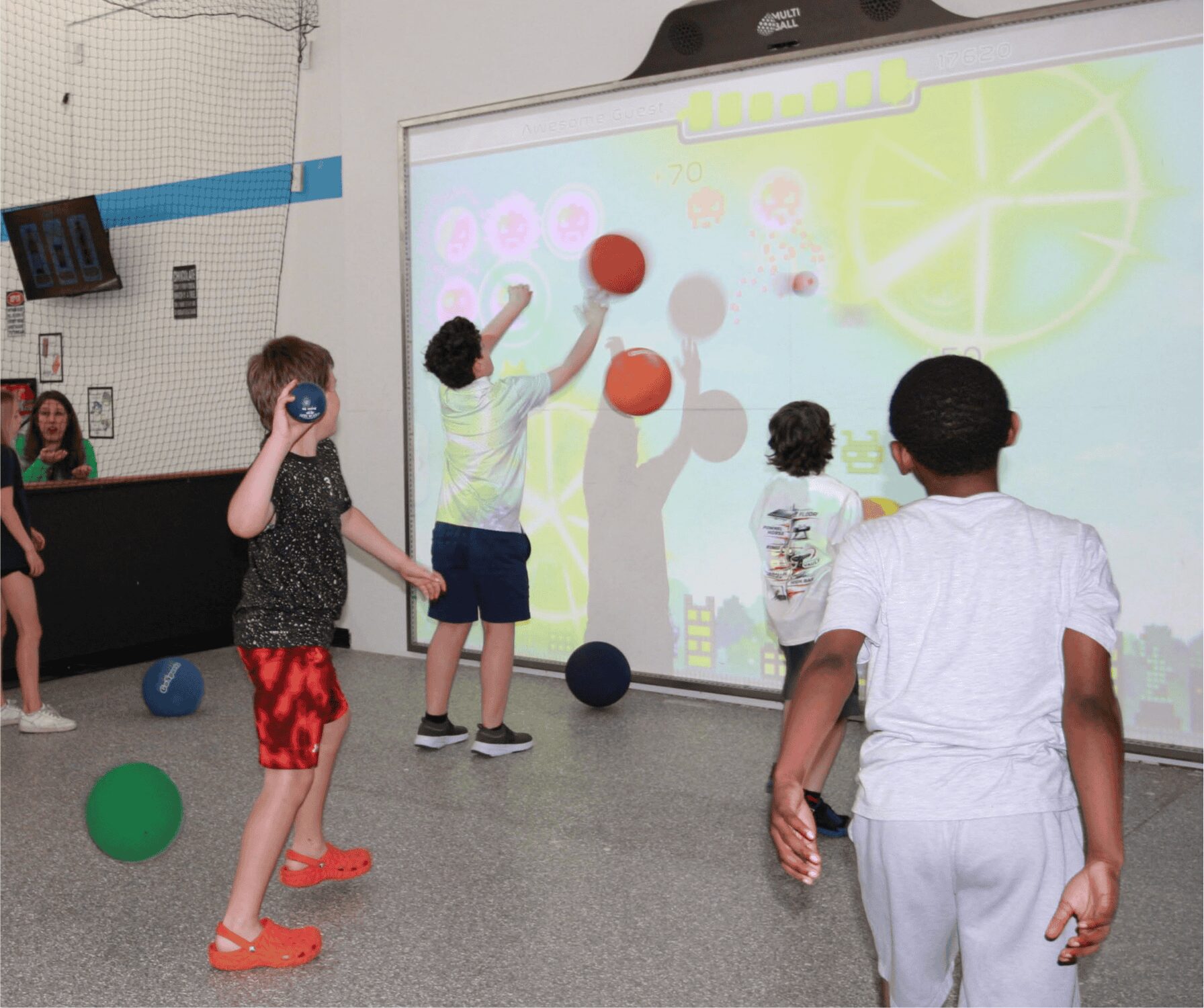 Children playing with large balls in front of an interactive whiteboard in a classroom.