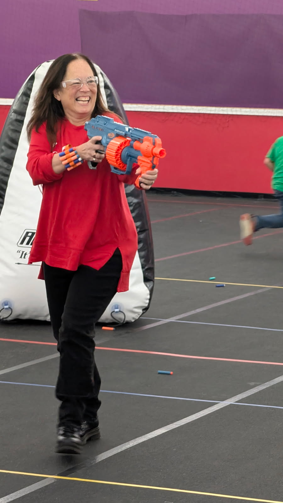 Woman smiling and holding a toy water gun indoors, wearing a red shirt and black pants.
