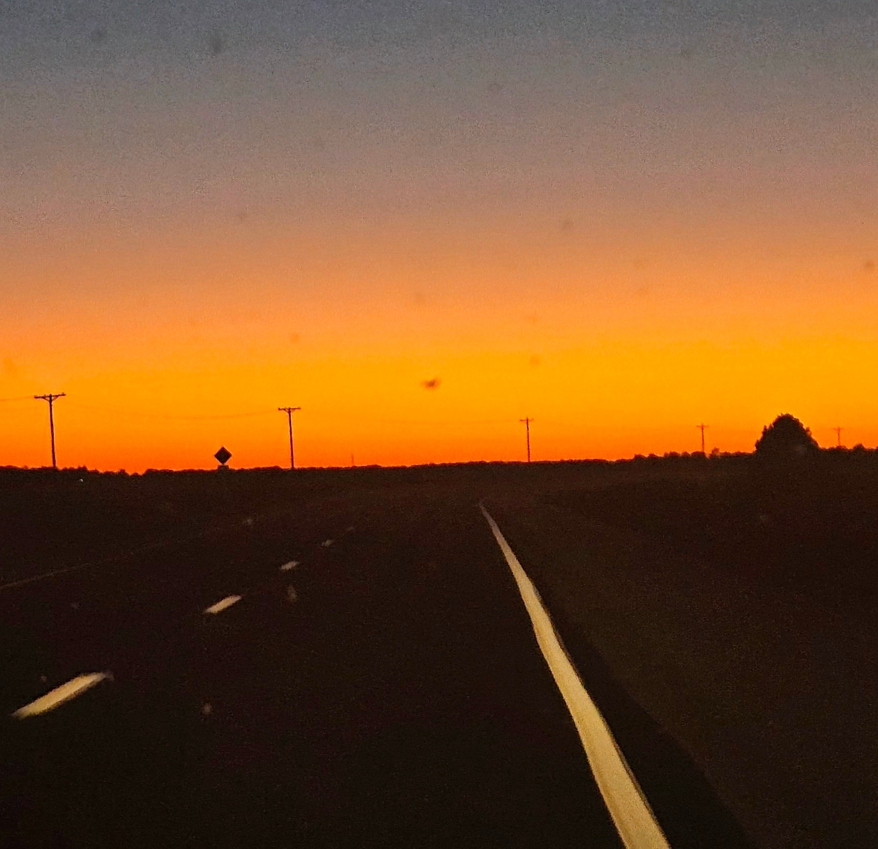 Road with lane markings extending toward horizon during sunset with colorful sky.