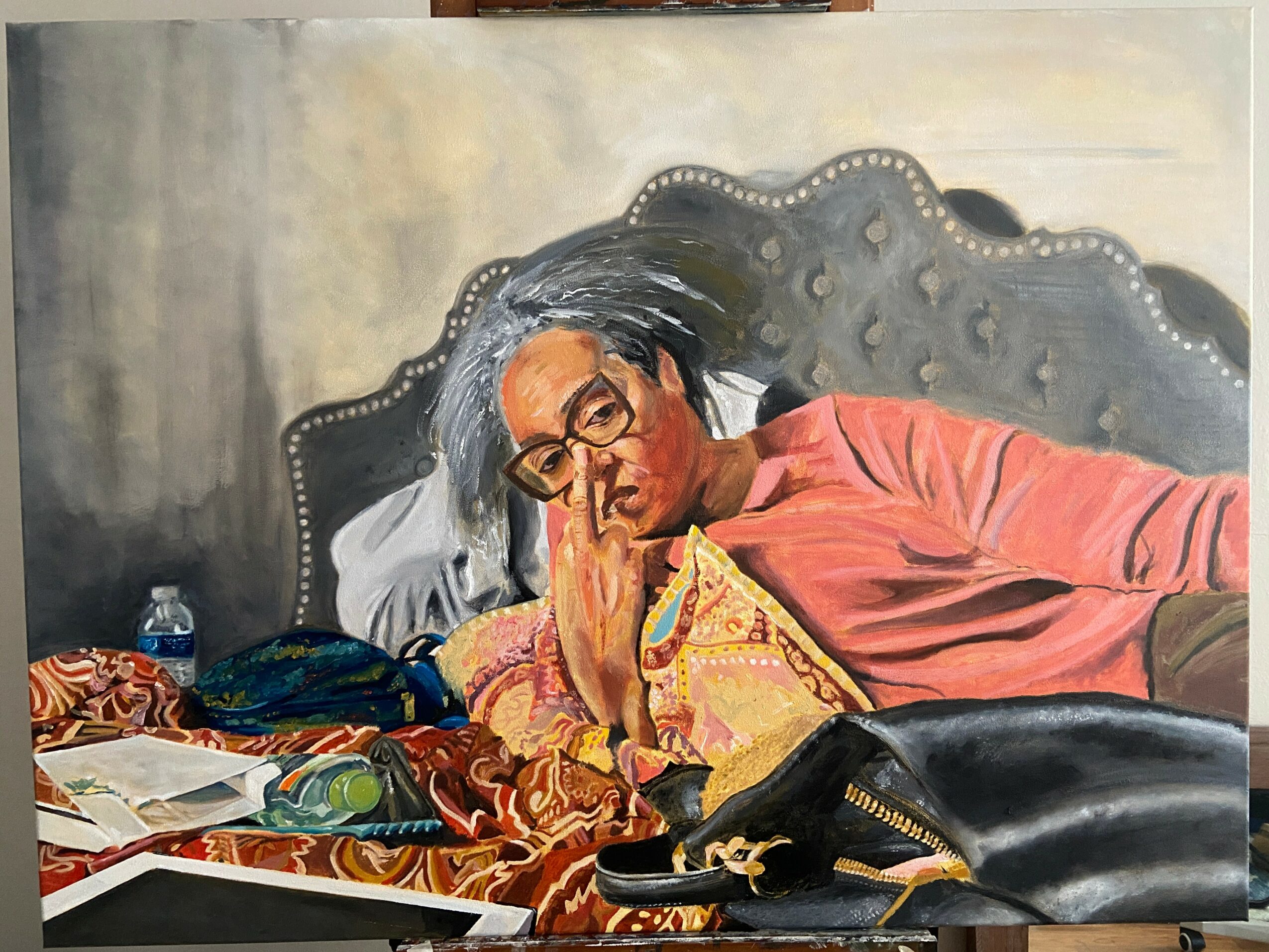 Person lying on bed with hand on face, wearing glasses and colorful clothing, surrounded by books and objects.