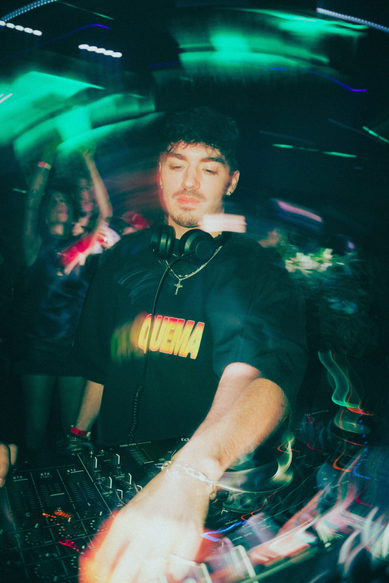 DJ with headphones at a turntable, motion blur with colorful lights, dark background, young man with dark hair, focused expression.