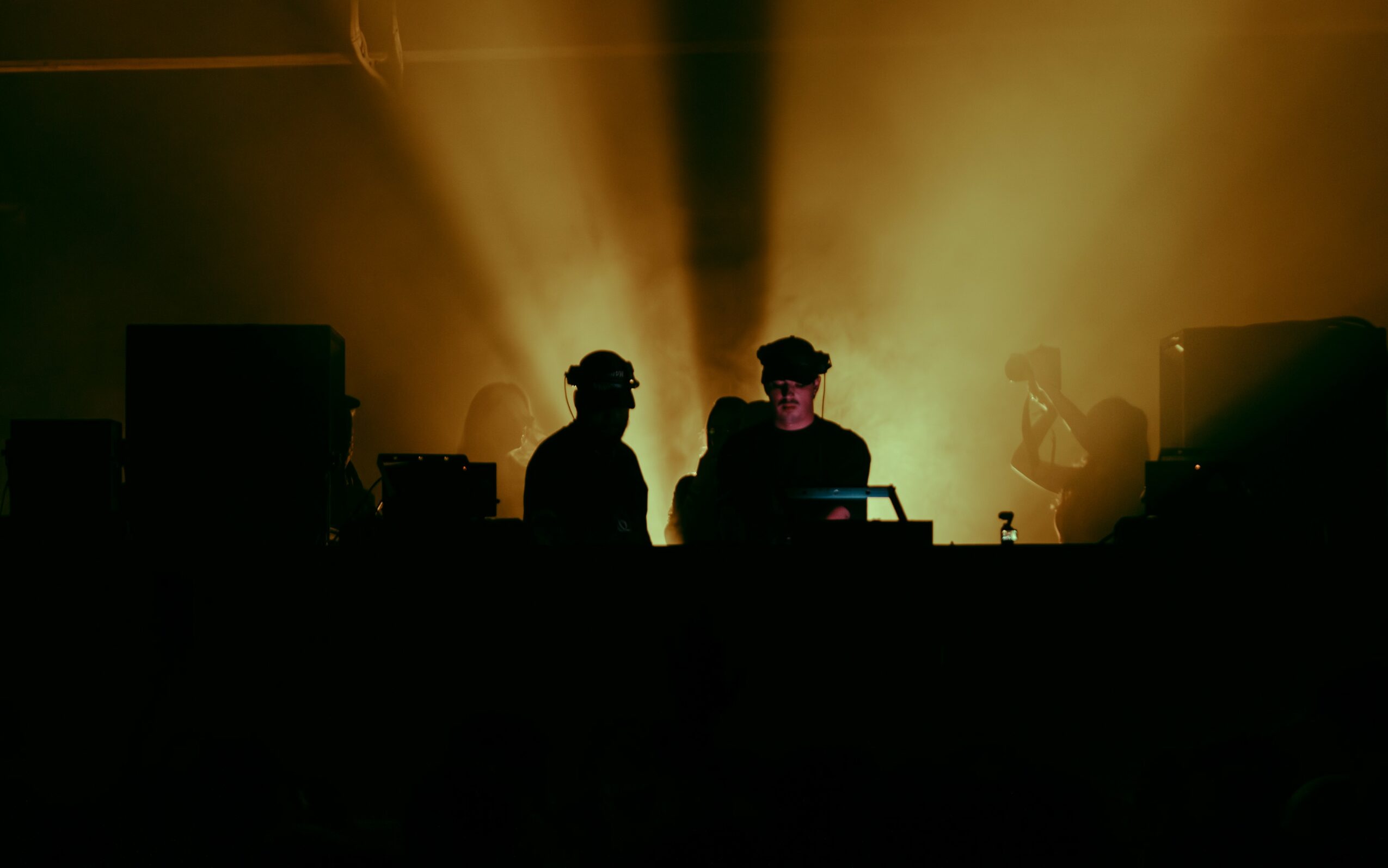 Silhouettes of people at a concert with bright yellow stage lights behind them.
