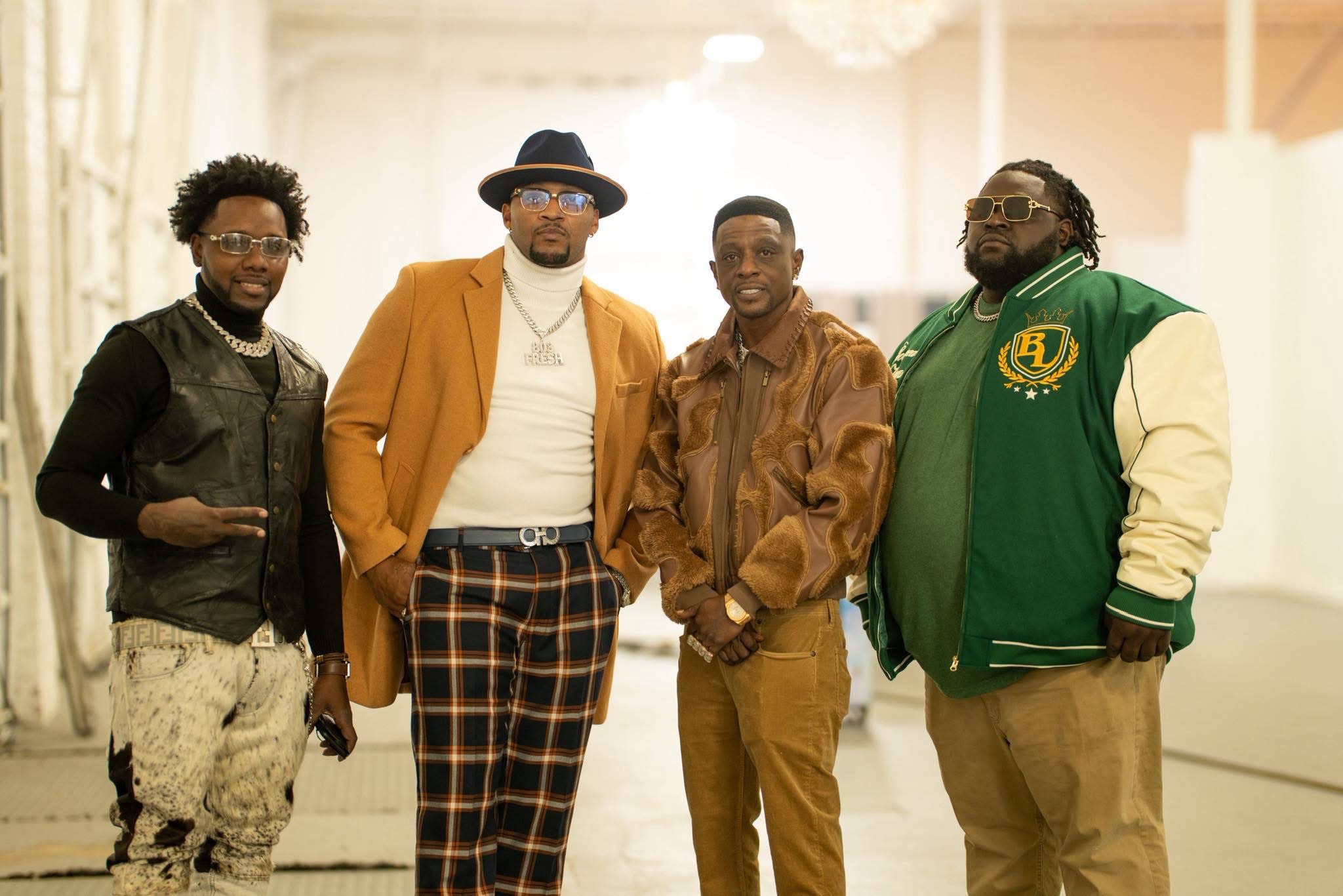 Four men standing together indoors, dressed in casual and stylish clothing, smiling at the camera.