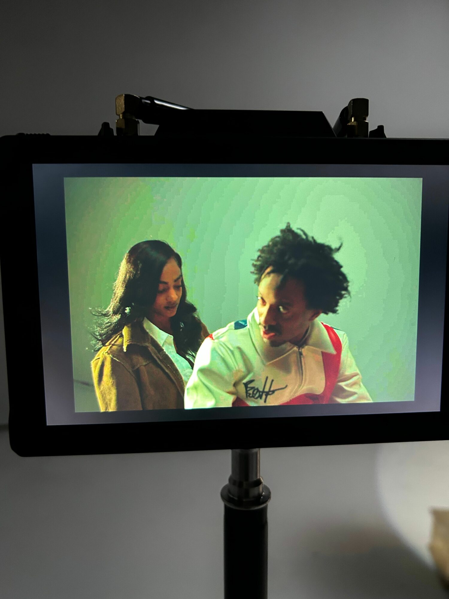 Two people, one with curly hair and the other with straight hair, facing each other against a green background.