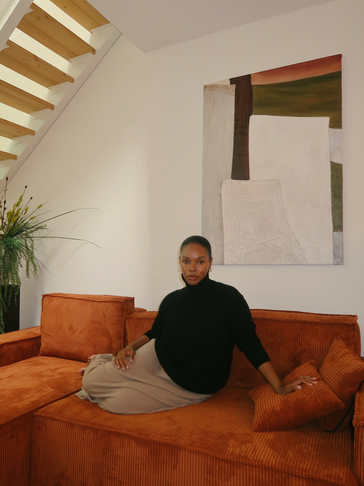 Woman sitting on a burnt orange sofa in a room with a large abstract painting on the wall.