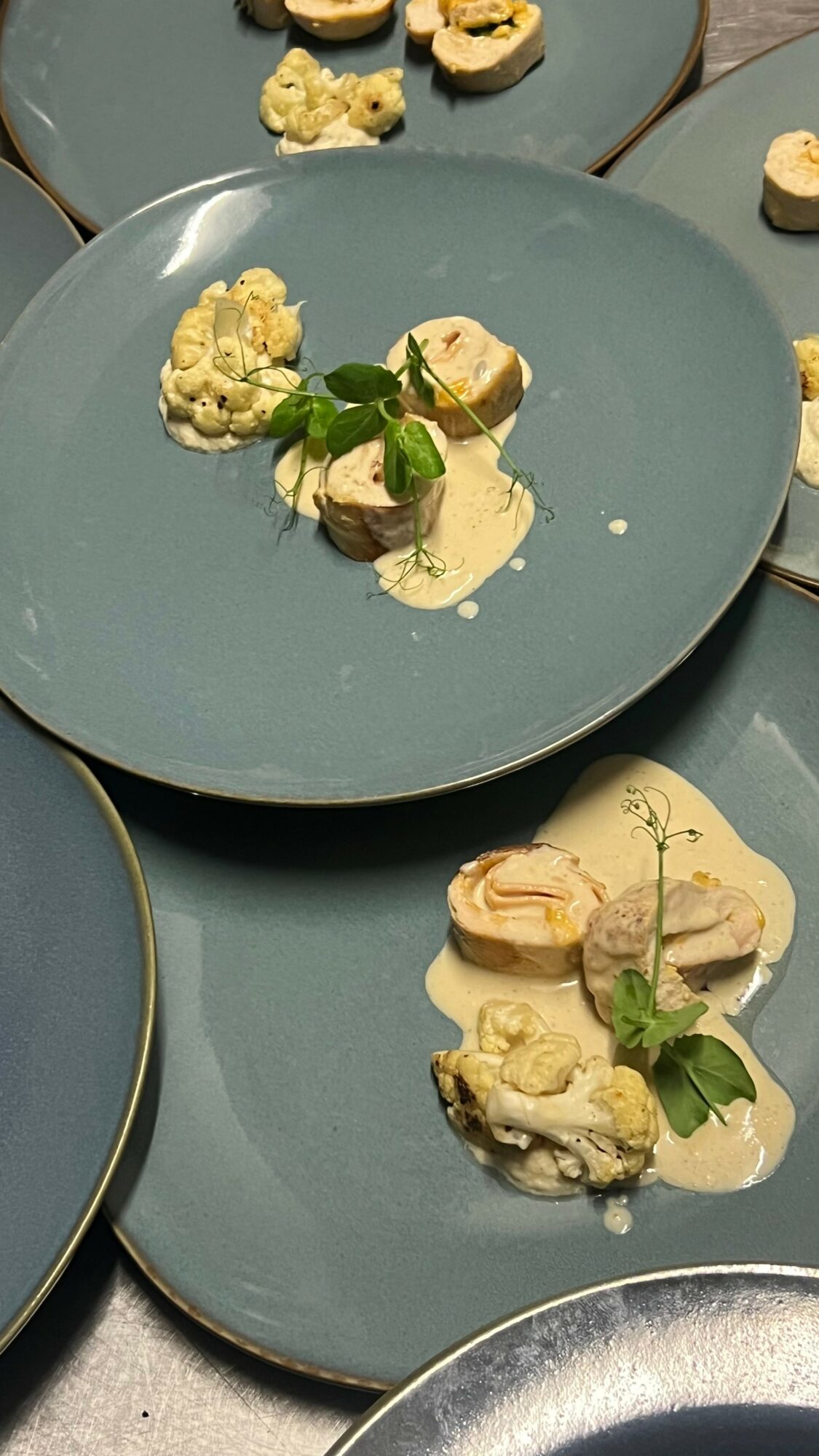 Multiple blue plates with small food portions, garnished with green herbs, arranged on a table.