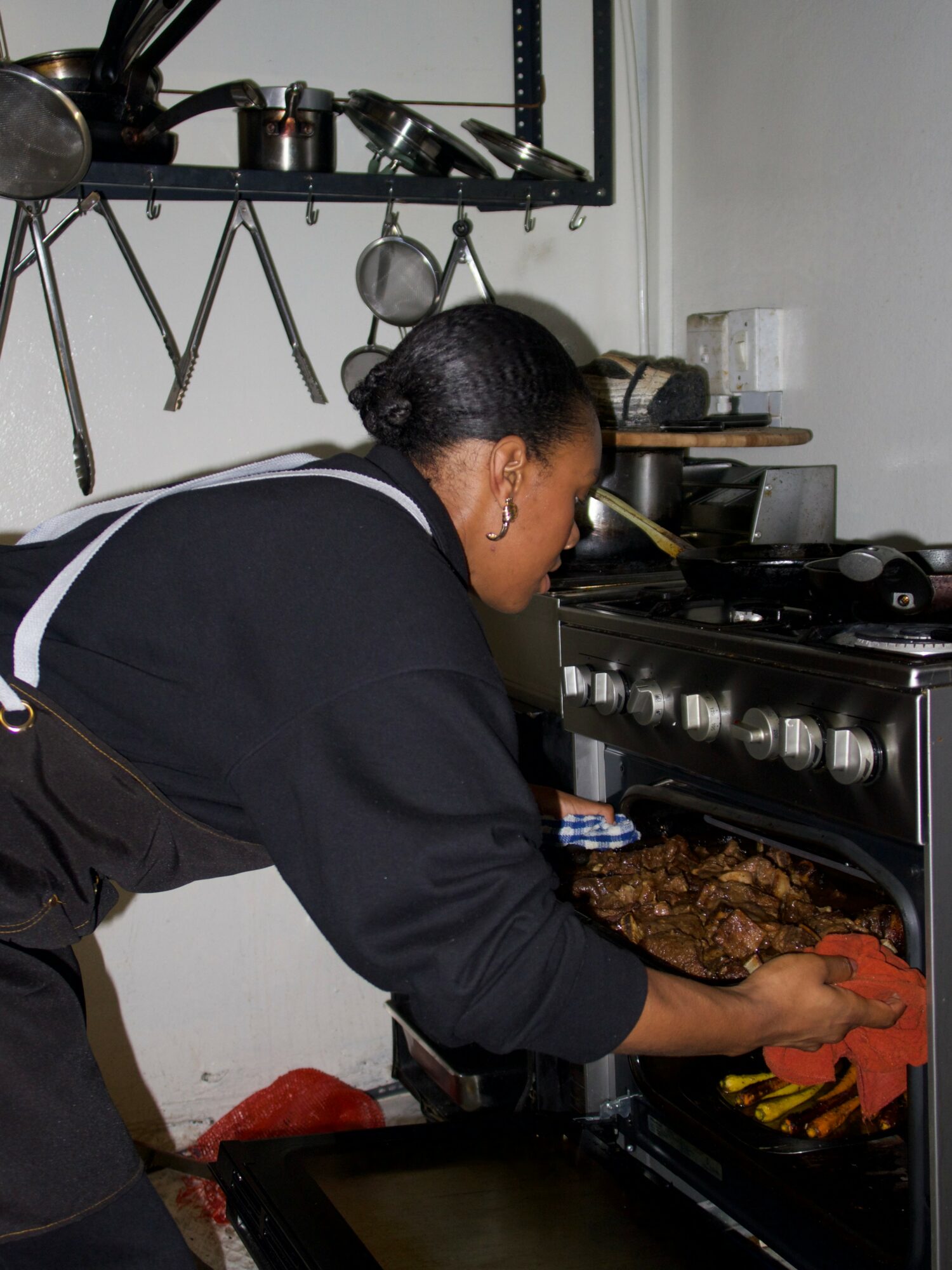 Person placing food in oven in a kitchen with utensils on a wall shelf.