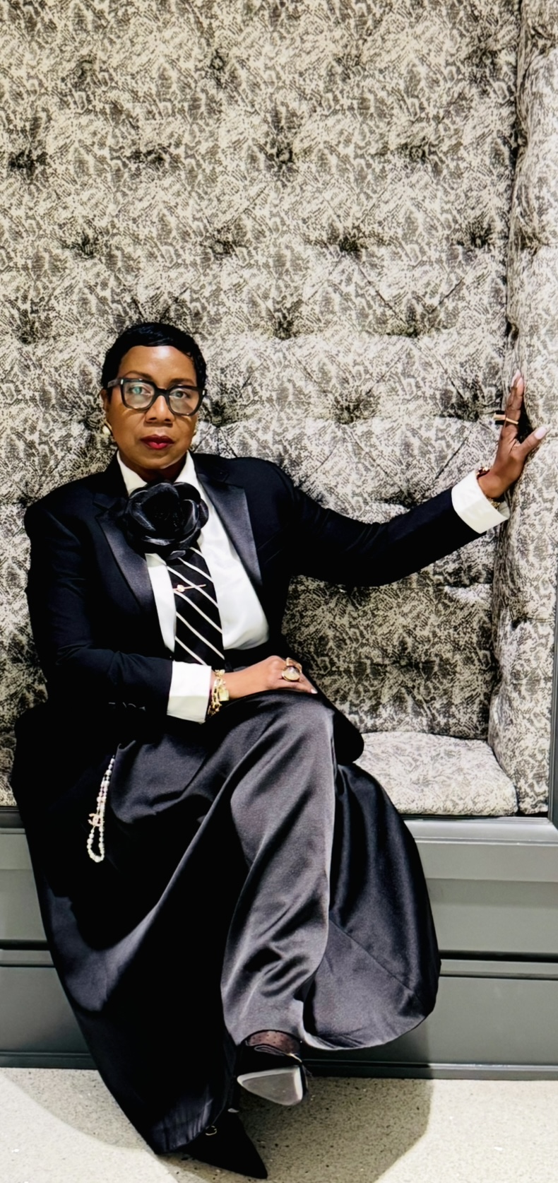 Person sitting on a bench, wearing formal attire, with a textured wall background.